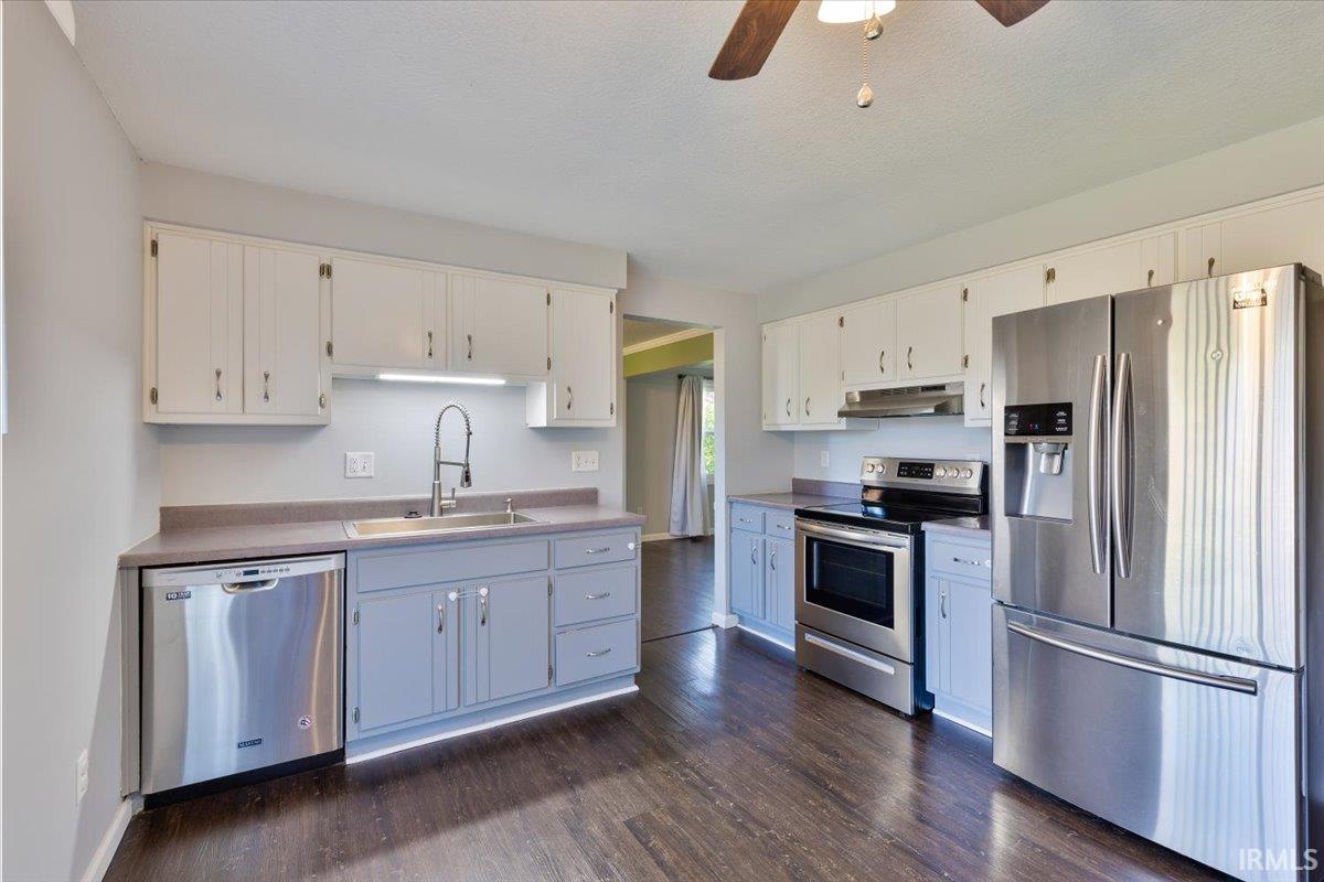 Kitchen featuring stainless steel appliances, wood-finish flooring, two-tone cabinetry, a ceiling fan, and under-cabinet lighting