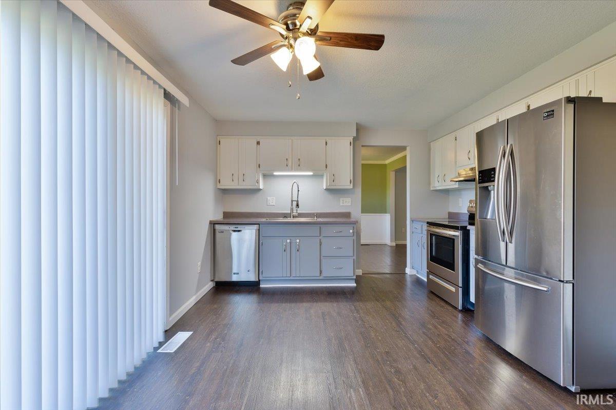 Kitchen featuring wood-finish flooring, stainless steel appliances, a ceiling fan with light fixture, and vertical blinds