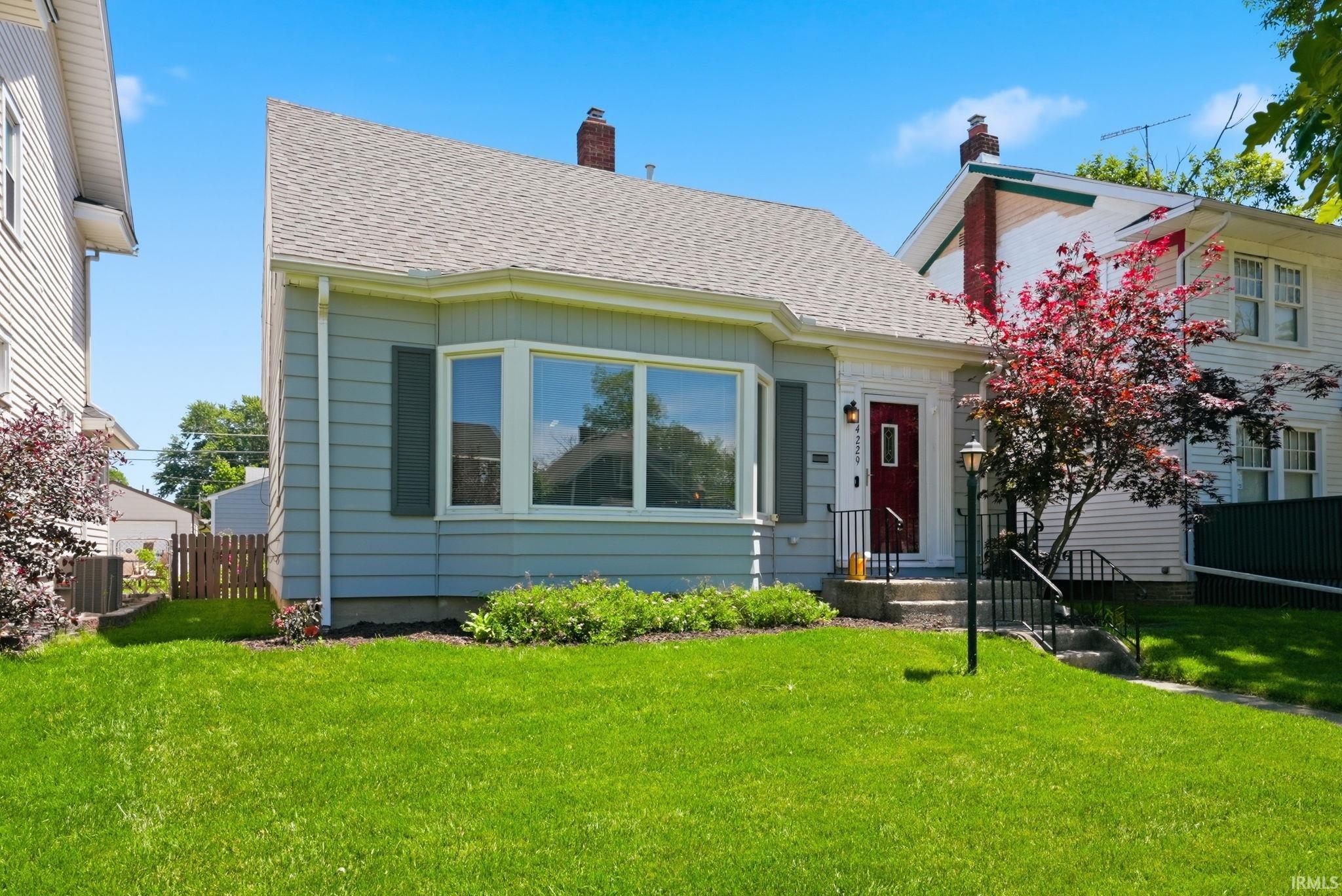 Light blue siding with a bay window, dark red entry door, and black window shutters