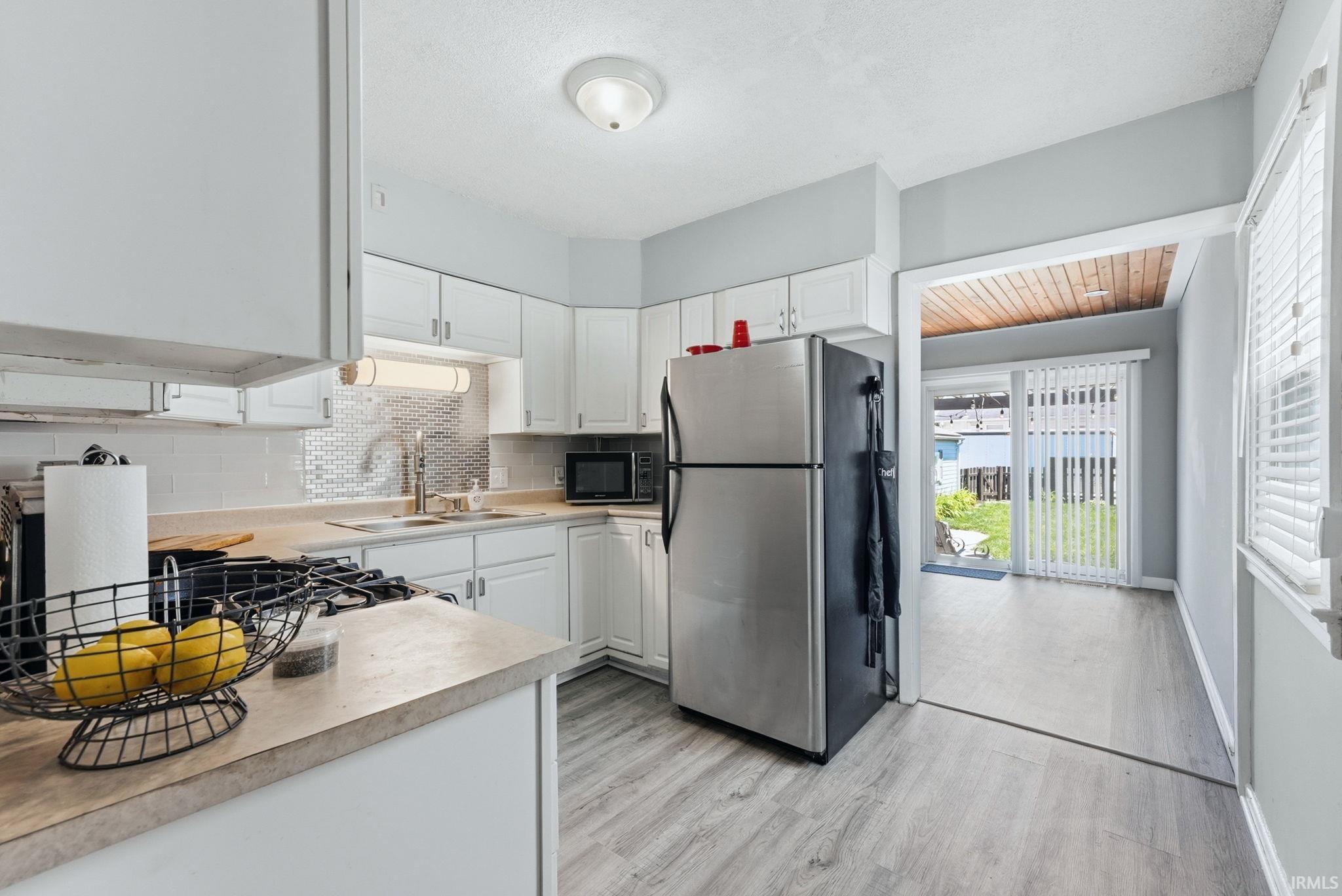 Kitchen featuring white cabinetry, light countertops, a mosaic tile backsplash, and wood-finish flooring