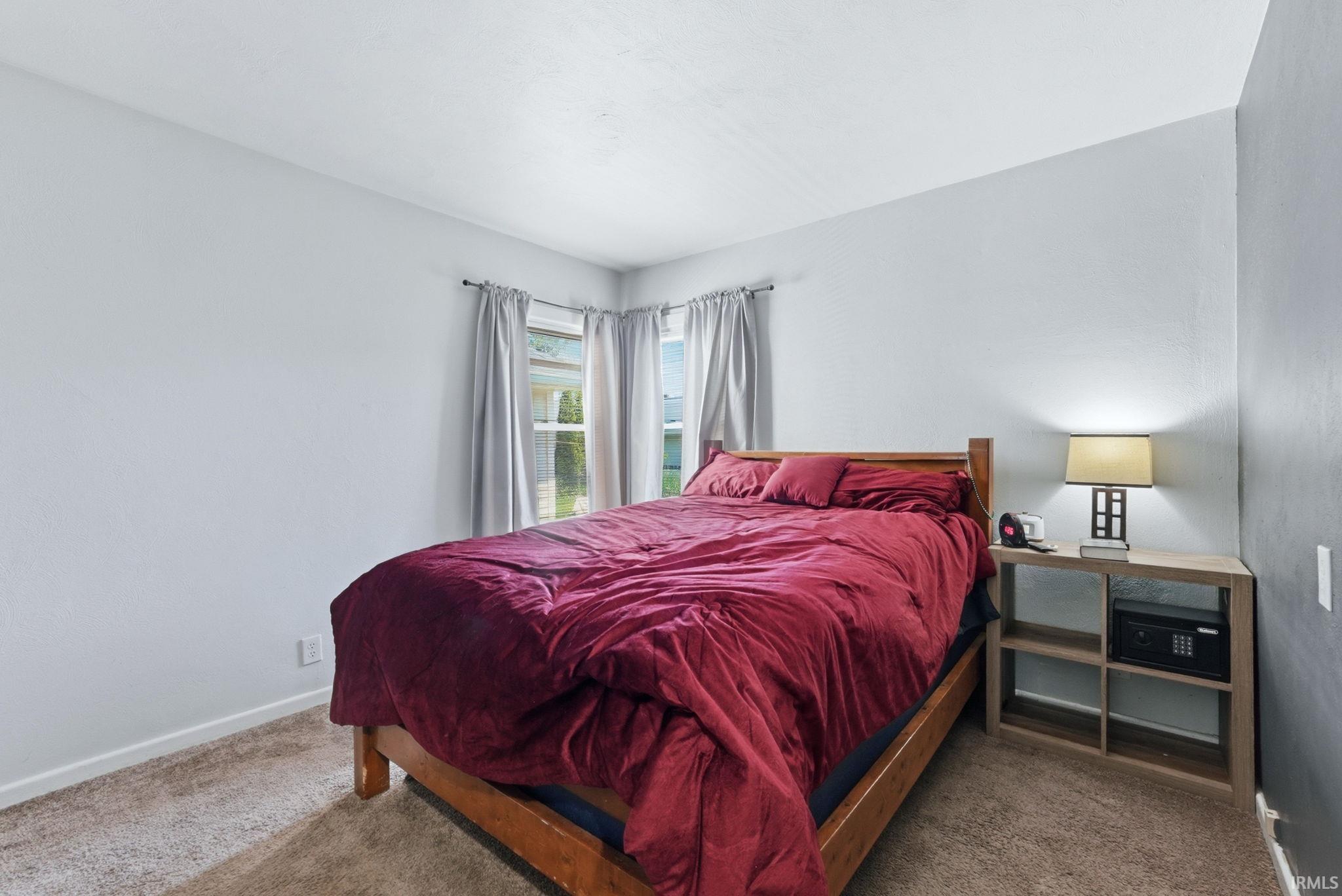 Carpeted bedroom featuring light gray walls, white trim, and two windows with drapes