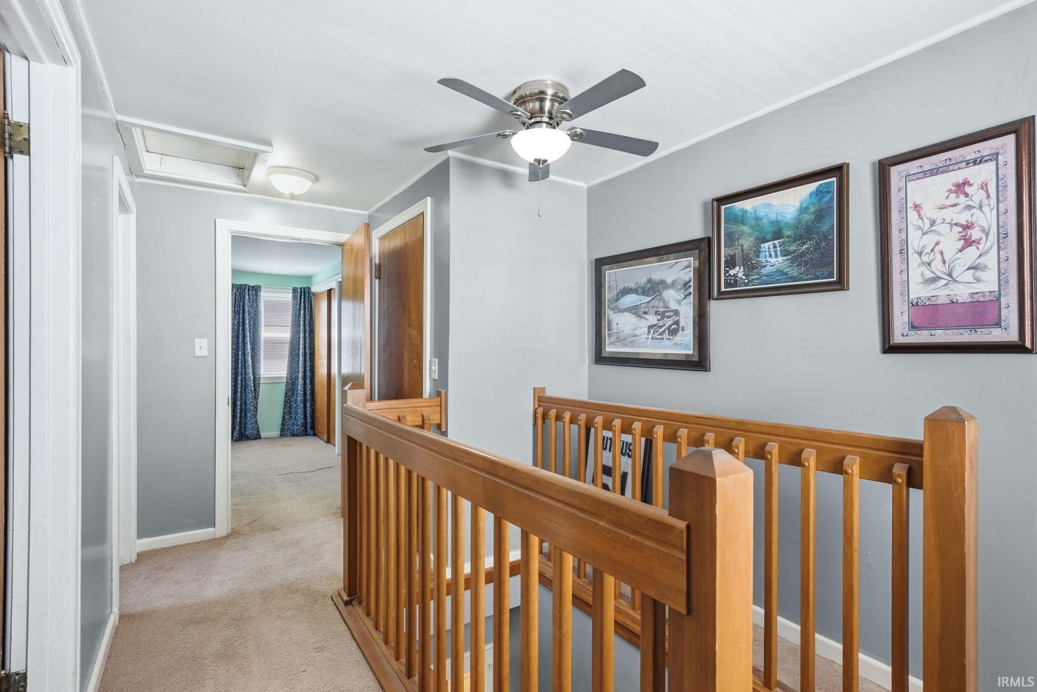 Upper-level hallway featuring a wood-finish banister, carpet flooring, and a ceiling fan with integrated lighting