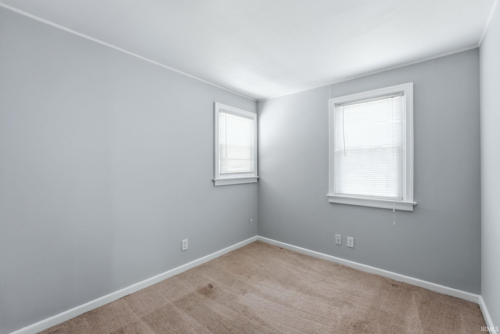 Light gray walls with white trim, two windows, and neutral carpeting