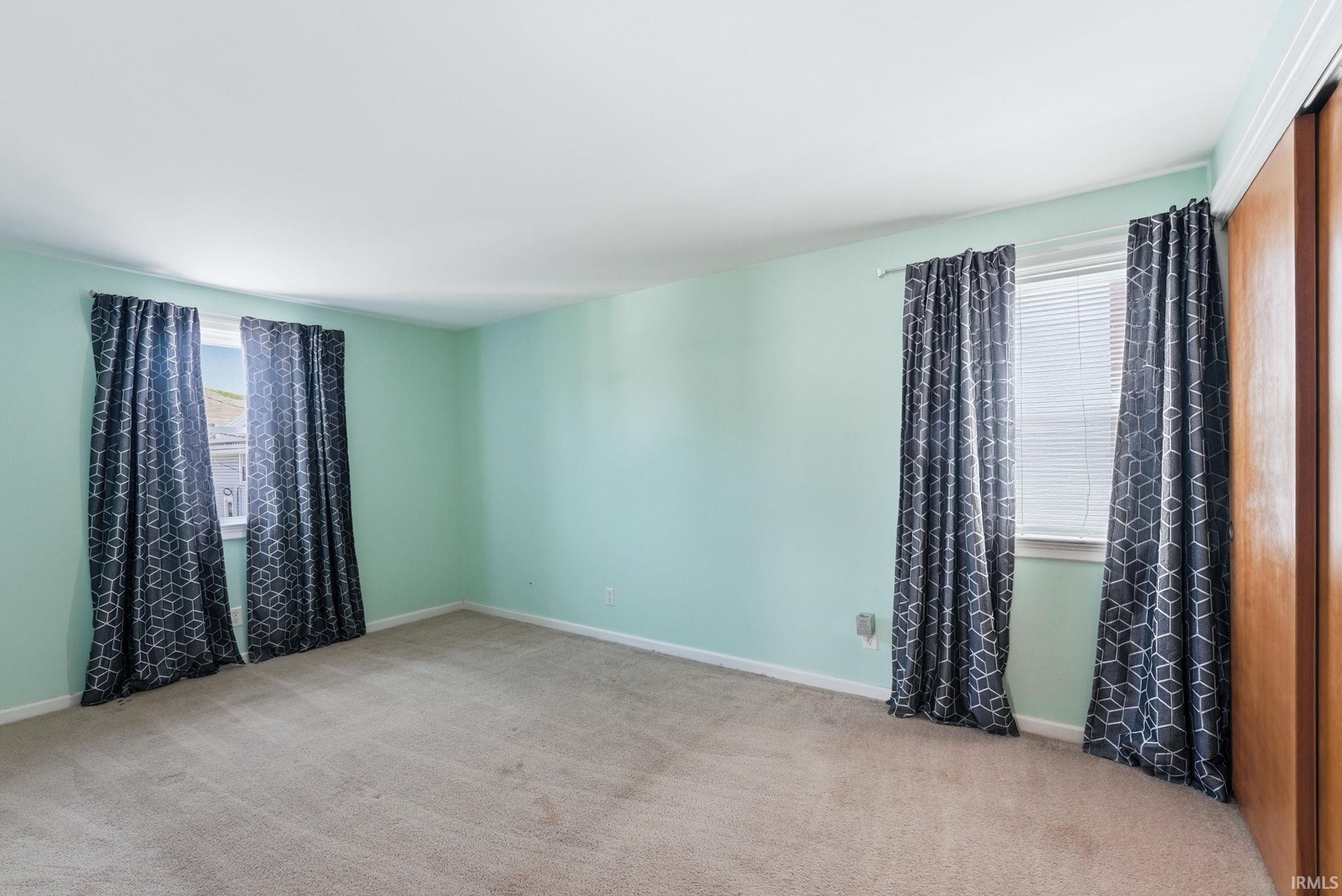 Spacious room with light green walls, two windows, carpet flooring, and a built-in wood-finish closet