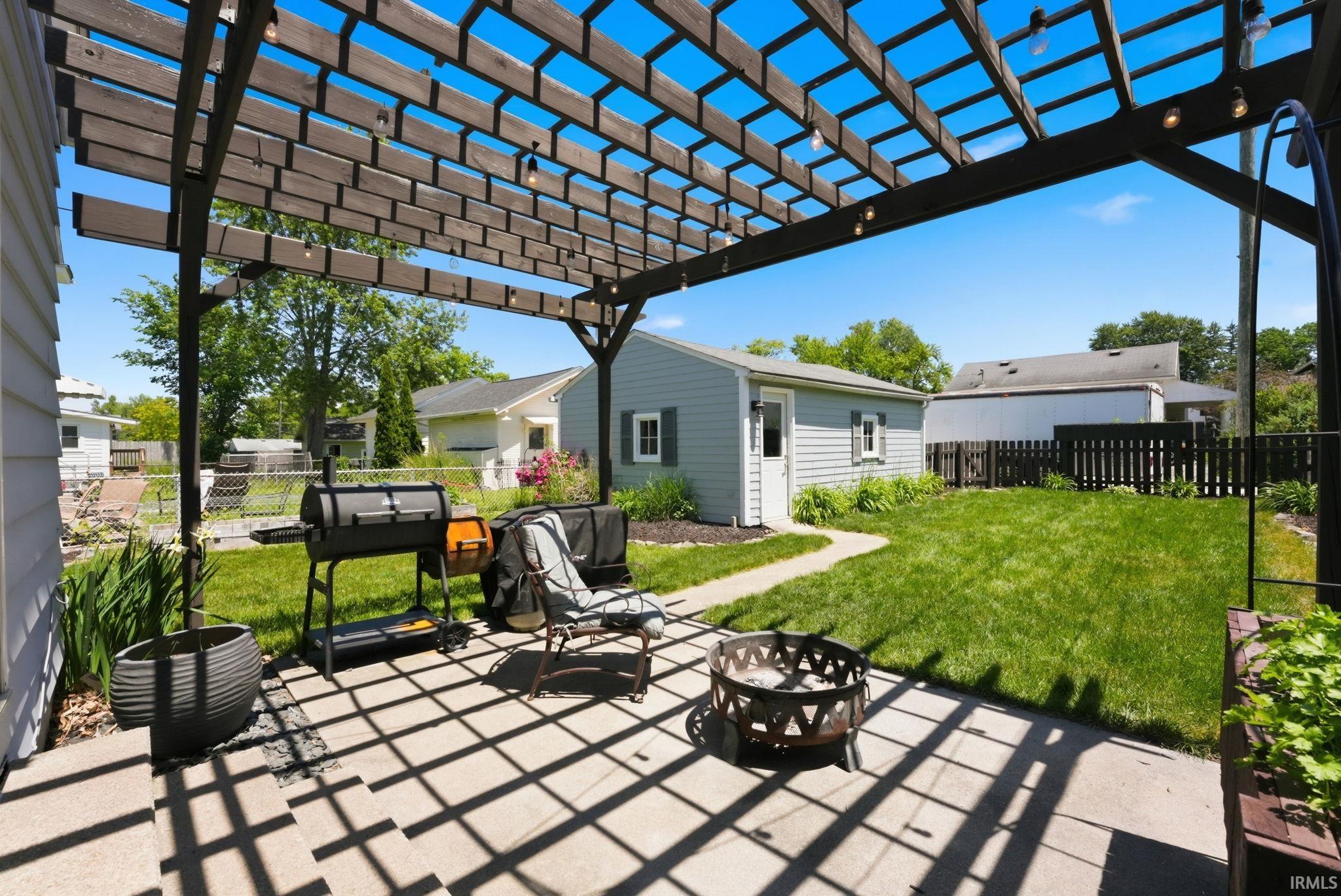 Paved patio with an open slat pergola and string lighting