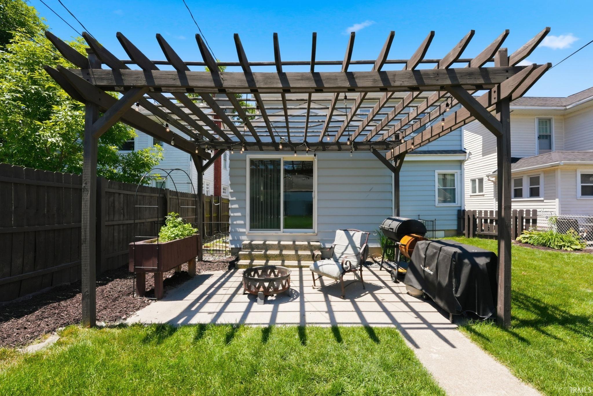 Expansive concrete patio featuring a dark wood pergola with string lighting