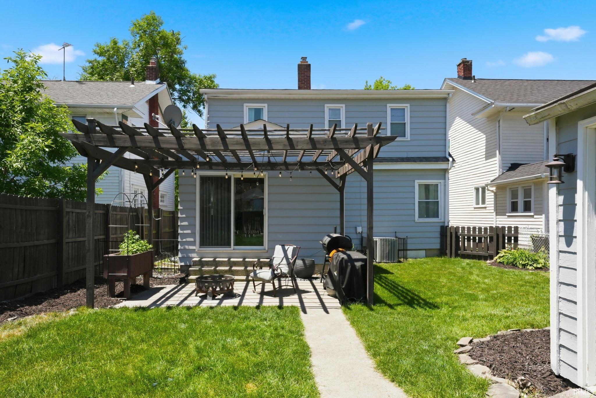 Rear exterior featuring a pergola-covered patio, sliding glass door access, and a fenced yard with a concrete pathway