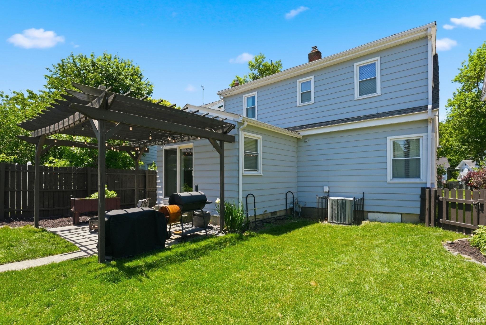 Spacious backyard featuring a dark wood pergola over a stone paver patio