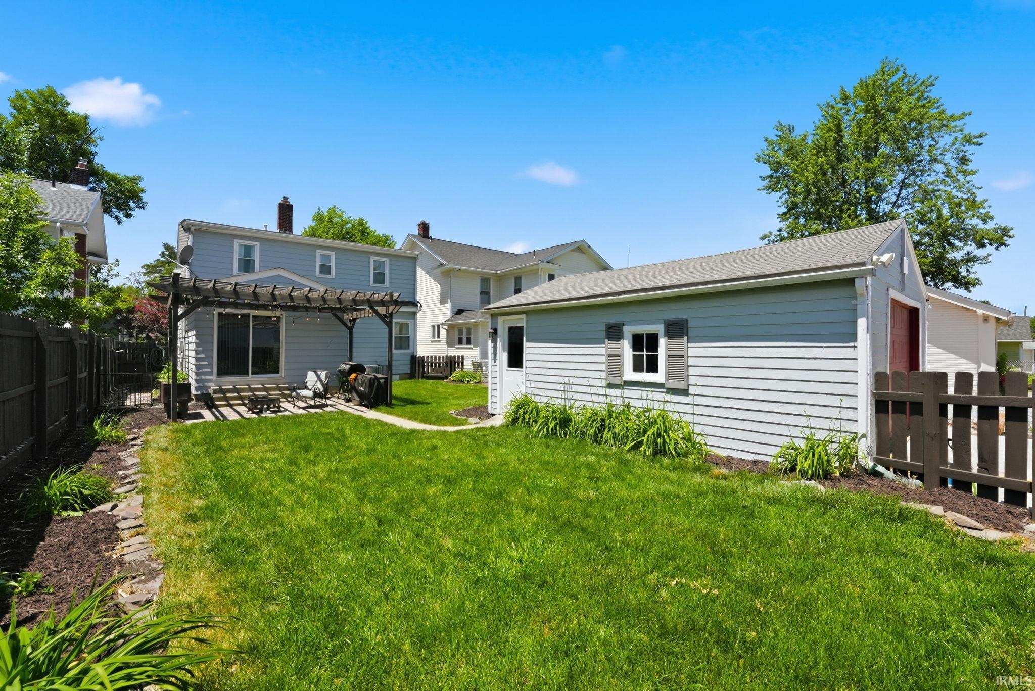 Expansive backyard featuring a manicured lawn, a detached storage building with siding, and a wooden pergola covering a patio area