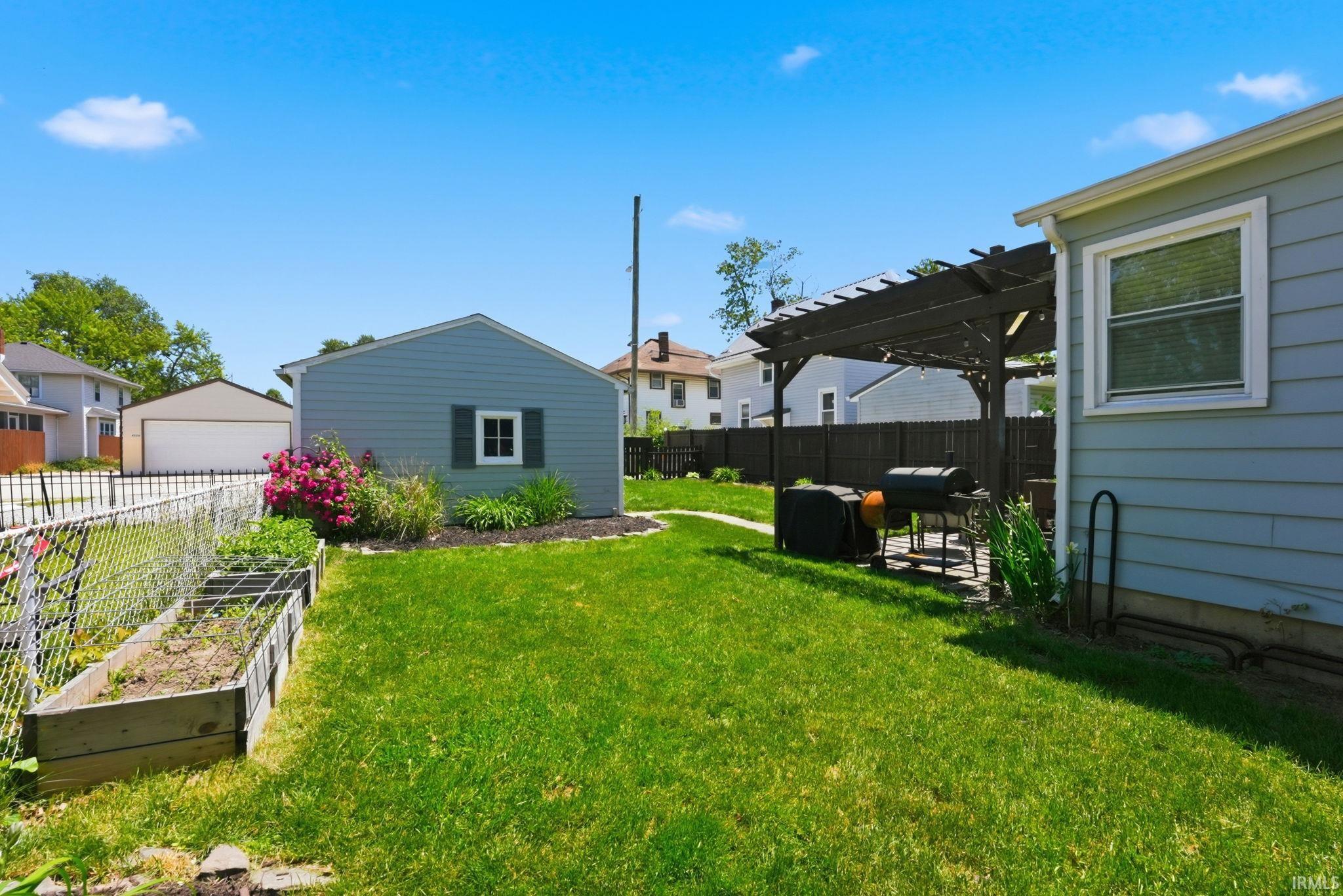 Expansive backyard featuring a lush lawn, a detached shed with siding, a raised garden bed, a paver patio with a pergola, and mature landscaping