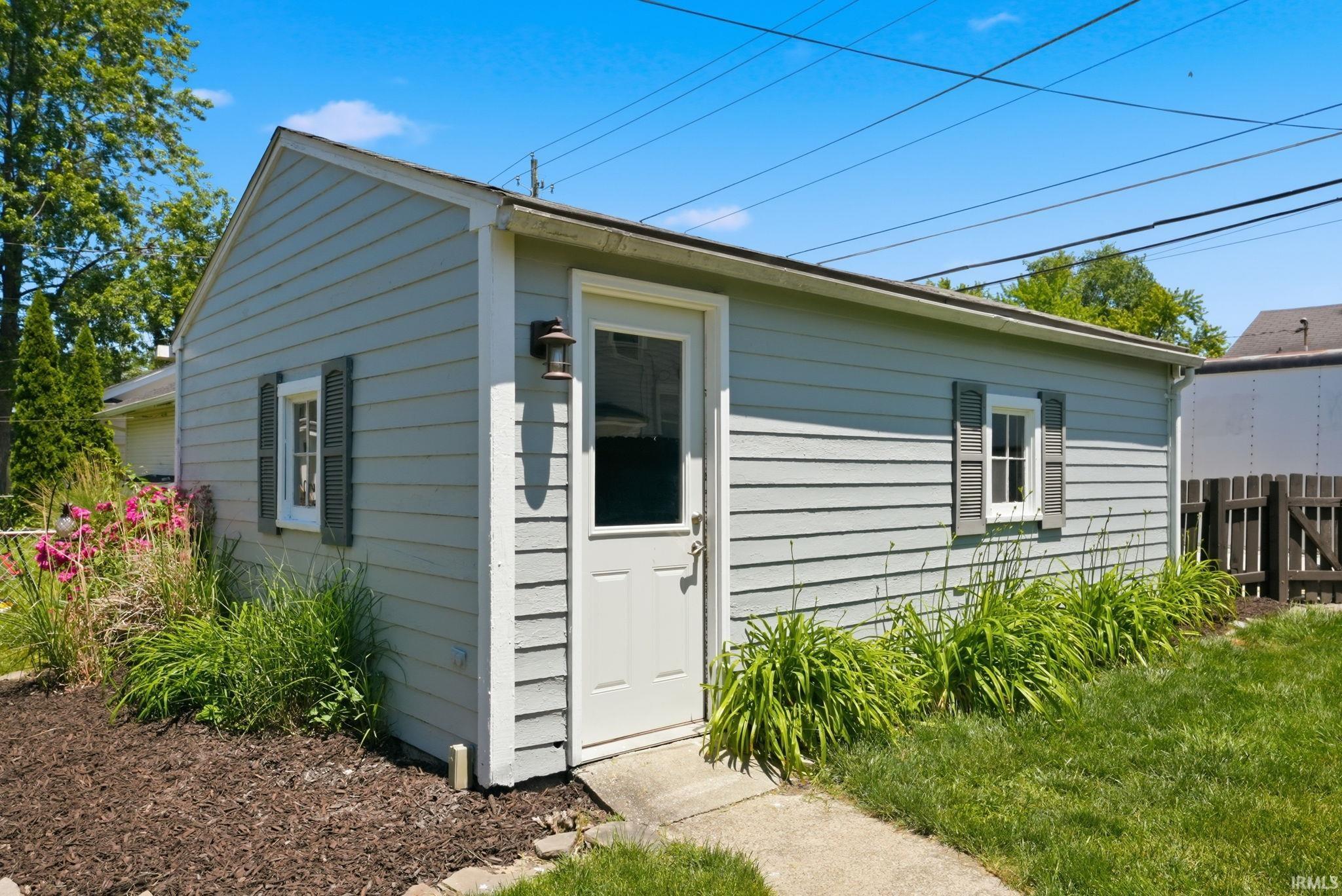 Detached structure featuring light gray siding, a white entry door, and two windows with dark shutters