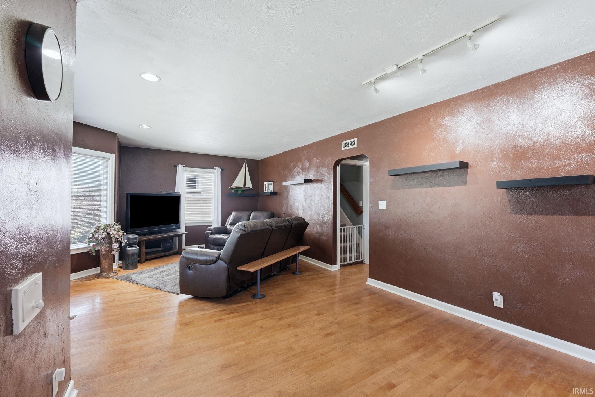 Living area featuring light wood-finish flooring, recessed ceiling lighting, track lighting, and an arched doorway