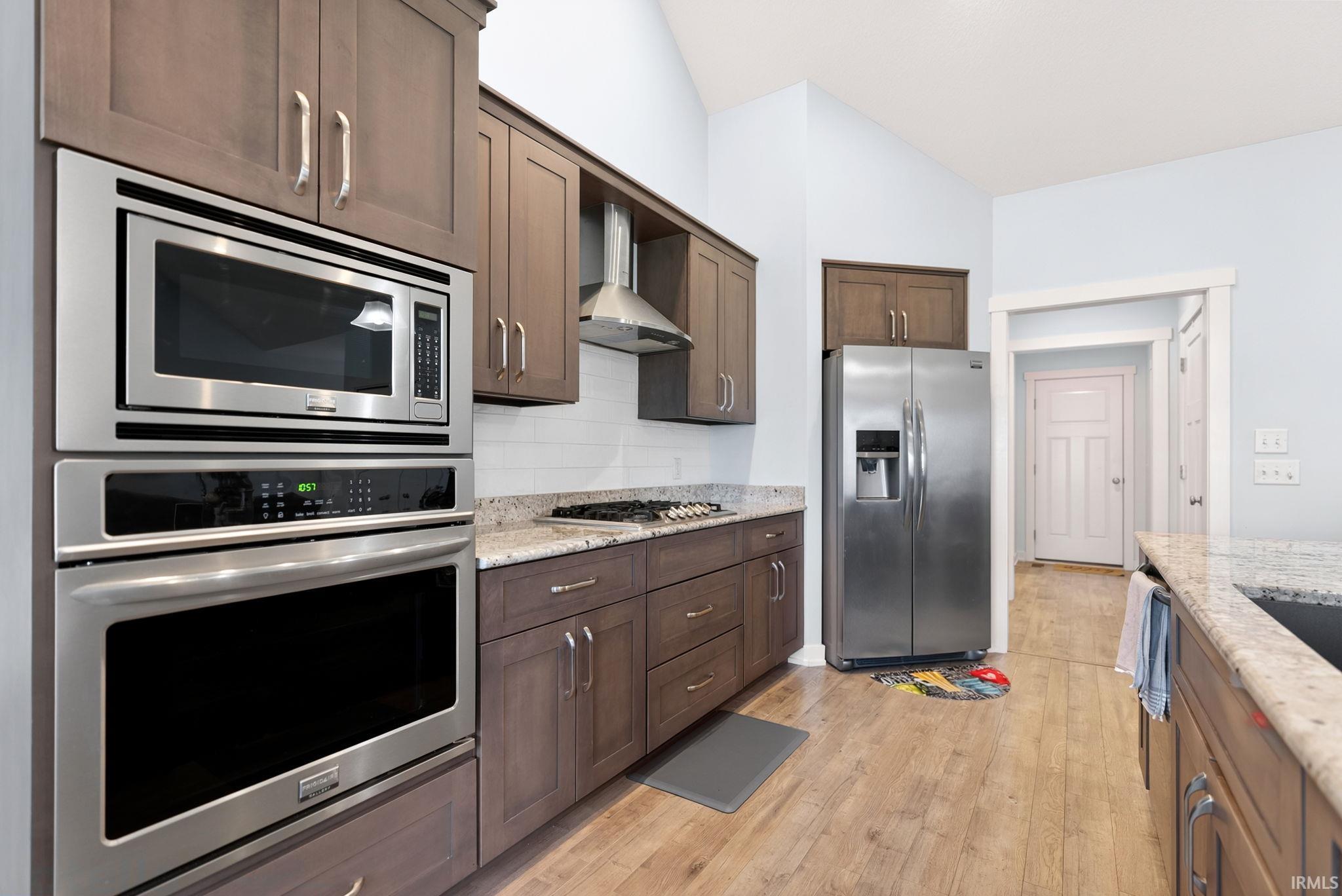 Modern kitchen featuring stainless steel appliances, wood-finish flooring, light-colored cabinetry, granite countertops, and a white subway tile backsplash