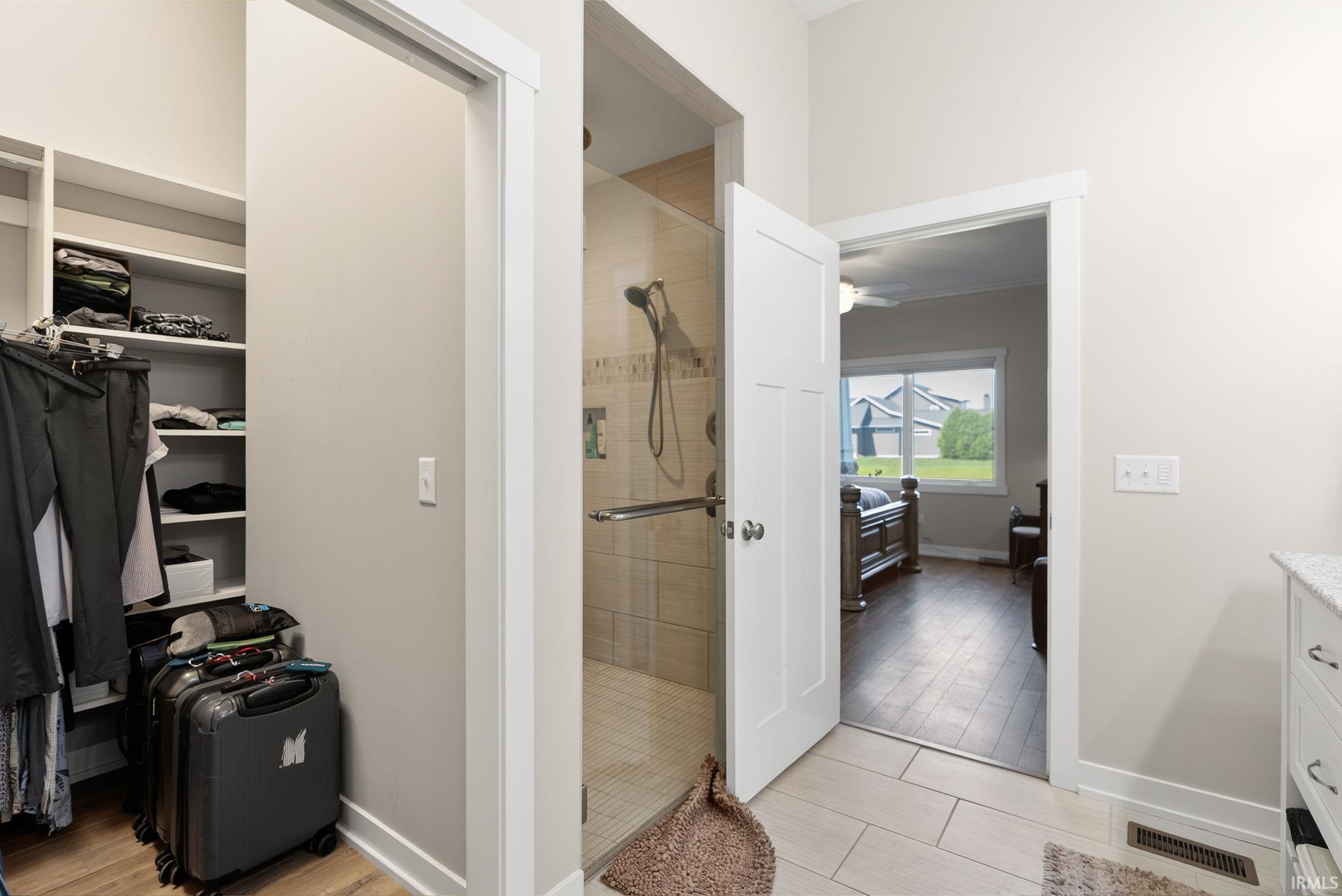 Walk-in closet with built-in shelving, glass-enclosed shower with tiled walls and floor, white paneled door, and tile flooring