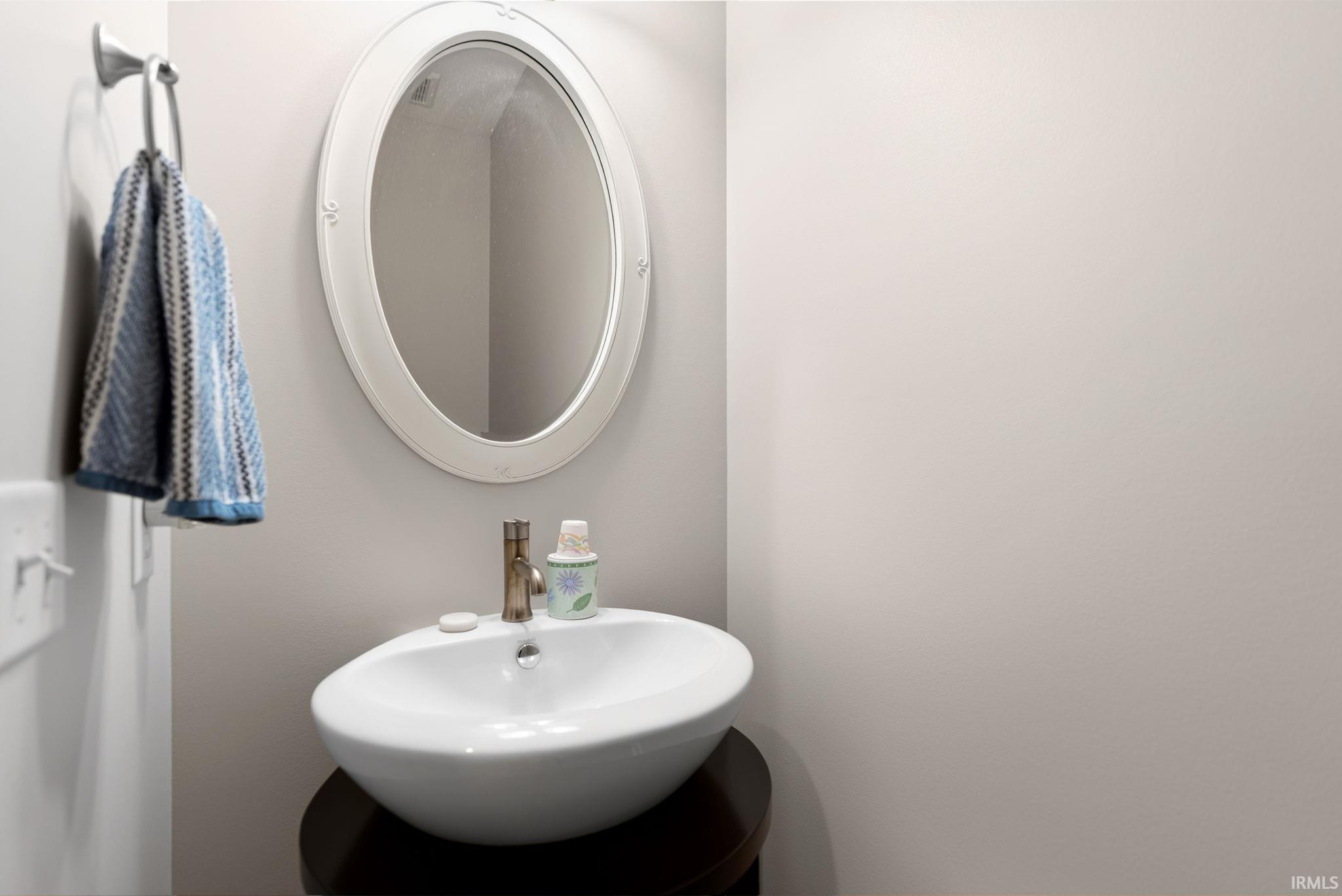 Pedestal vessel sink with a contemporary faucet, complemented by an oval wall mirror with a decorative frame