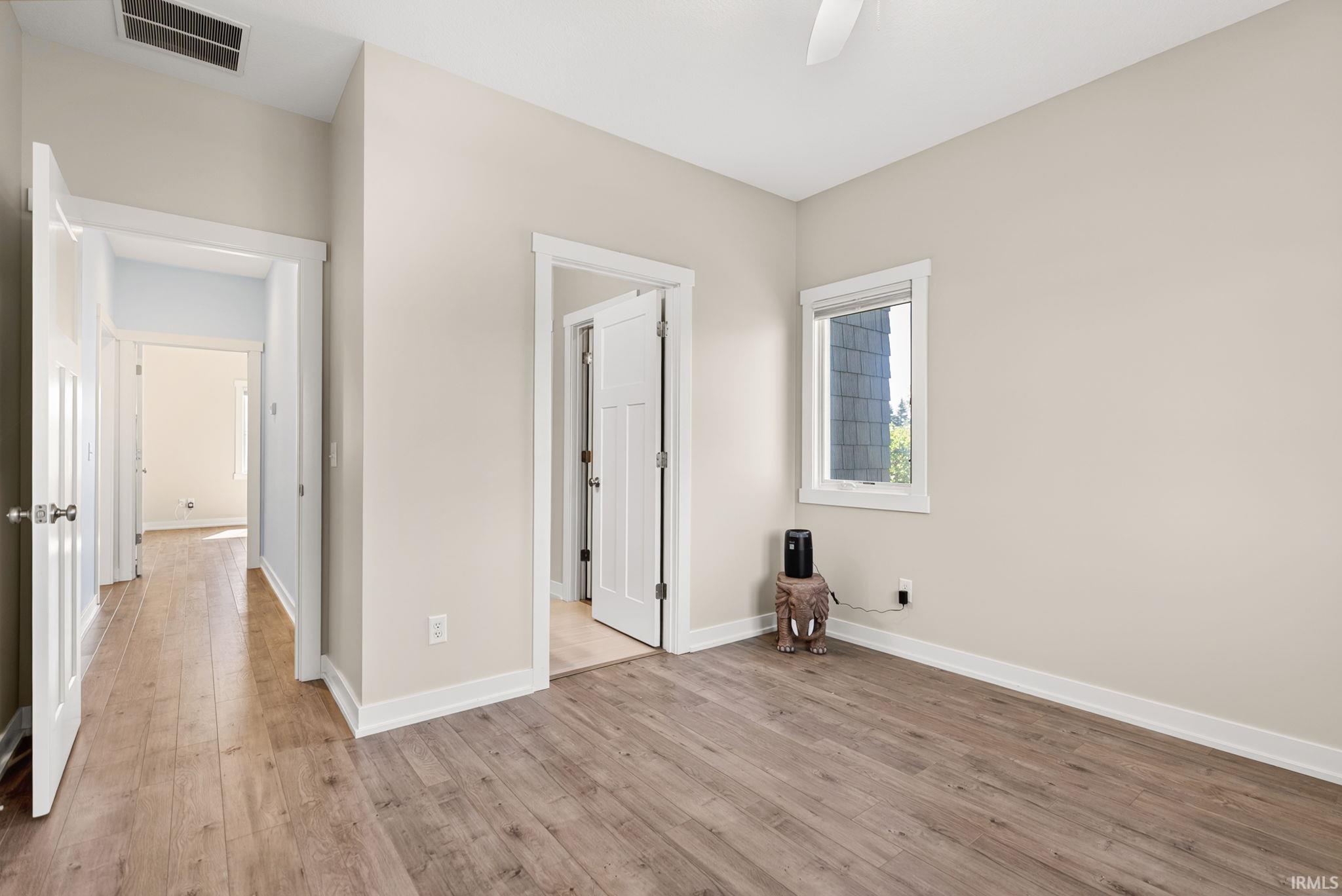 Spacious room featuring wood-finish flooring, neutral wall tones, crisp white trim, and a ceiling fan