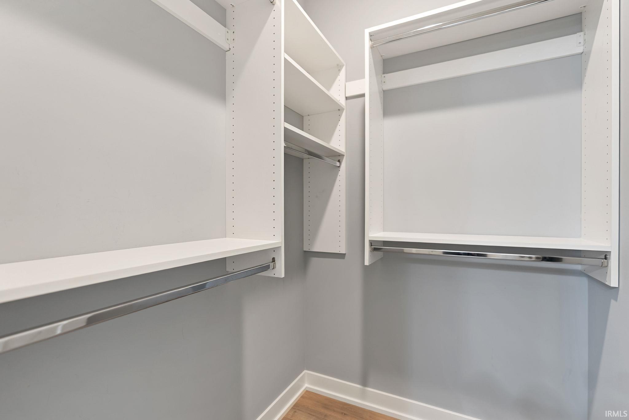 Walk-in closet featuring white built-in shelving, chrome hanging rods, light gray wall paint, and wood-finish flooring