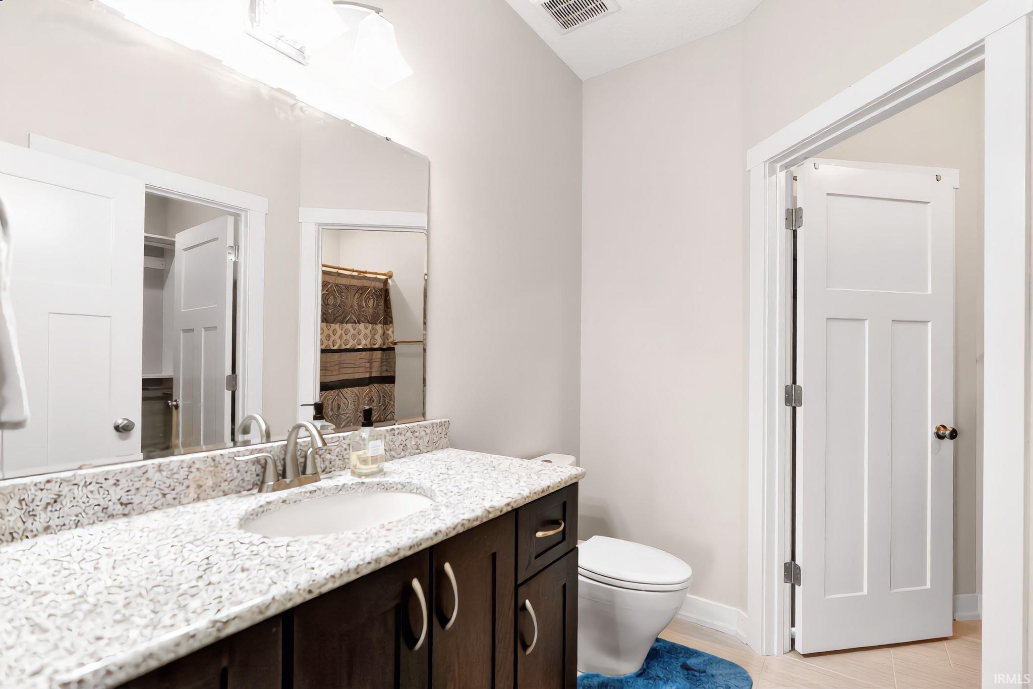 Bathroom featuring a dark wood-finish vanity with a single basin, a speckled light-toned countertop, and a large wall-mounted mirror