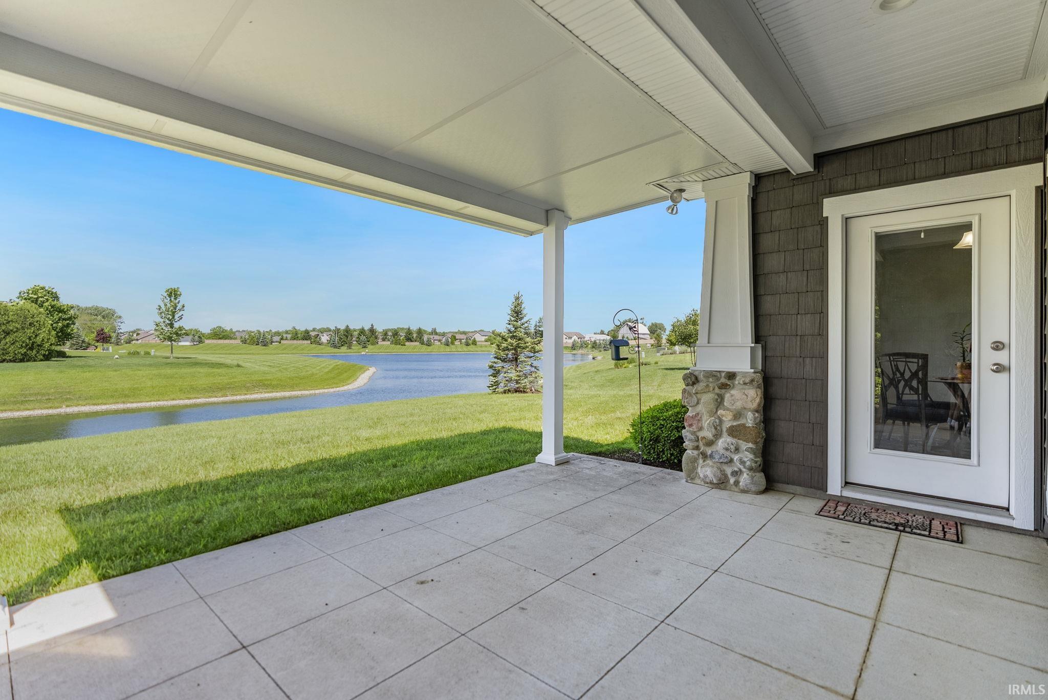 Covered outdoor patio with square concrete pavers, overlooking a large body of water and manicured green space
