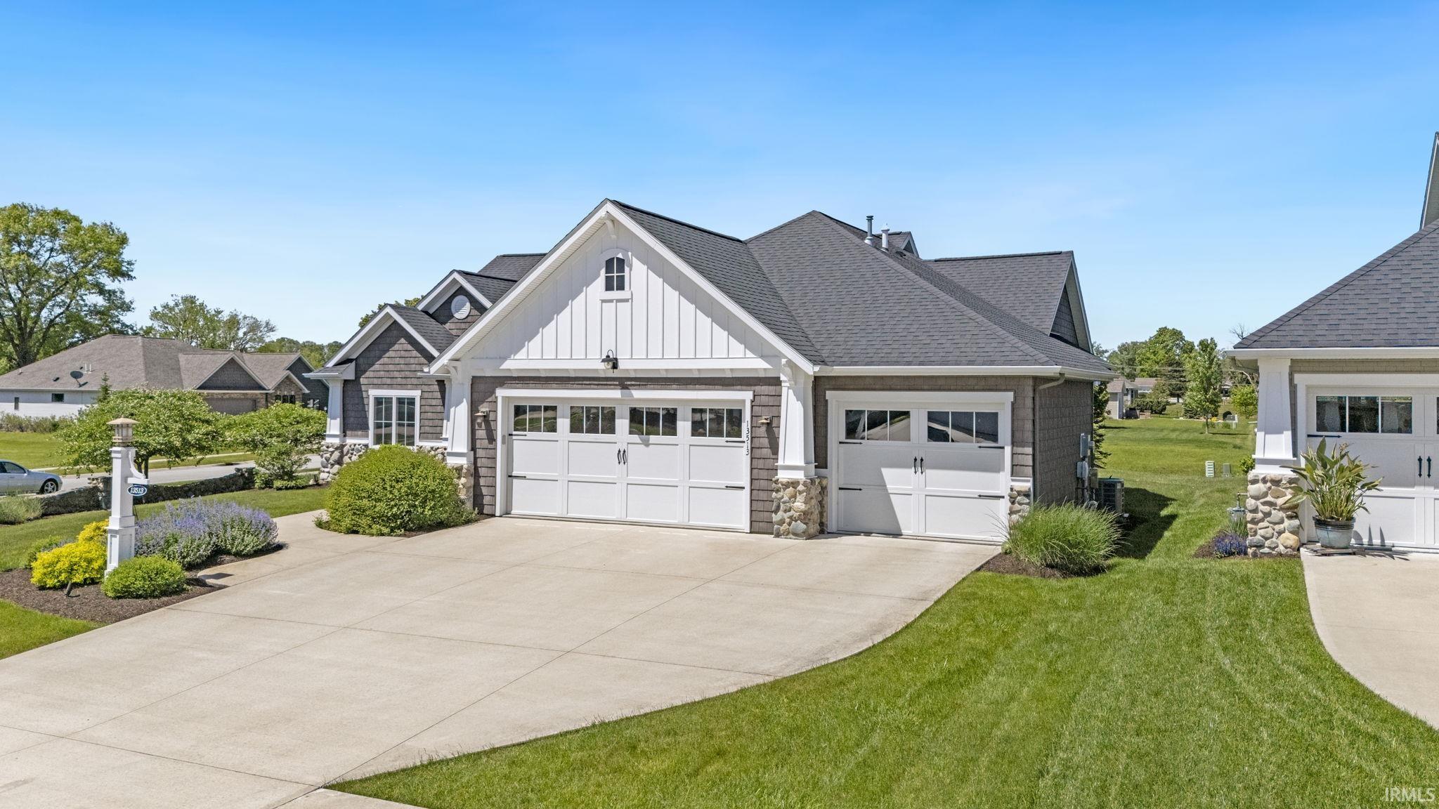Multi-car garage featuring white paneled doors with window accents, stone column bases, and a board and batten gable