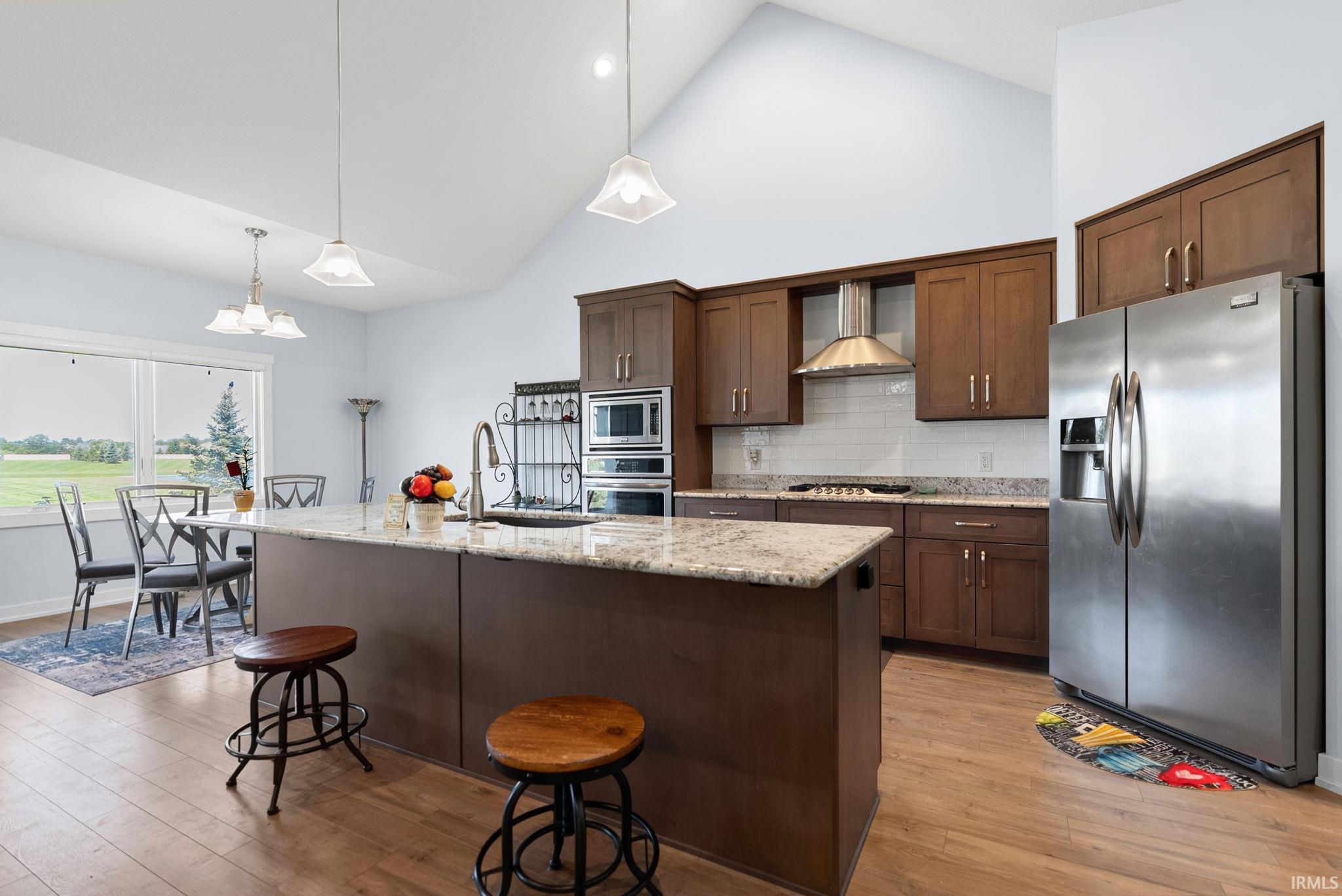Vaulted ceiling kitchen featuring wood-finish flooring, a central island with a light-toned countertop, stainless steel appliances, and wood cabinetry