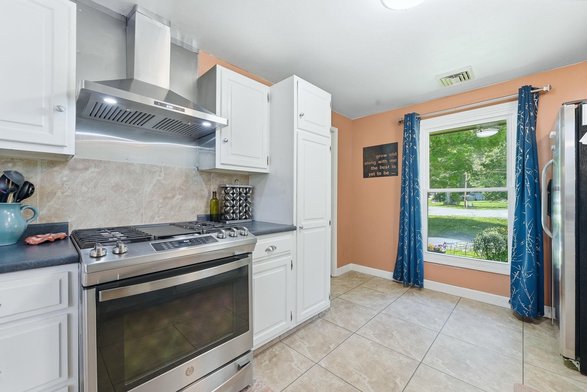 Kitchen featuring a stainless steel range with a coordinating range hood, stone-finish tile backsplash, and white cabinetry
