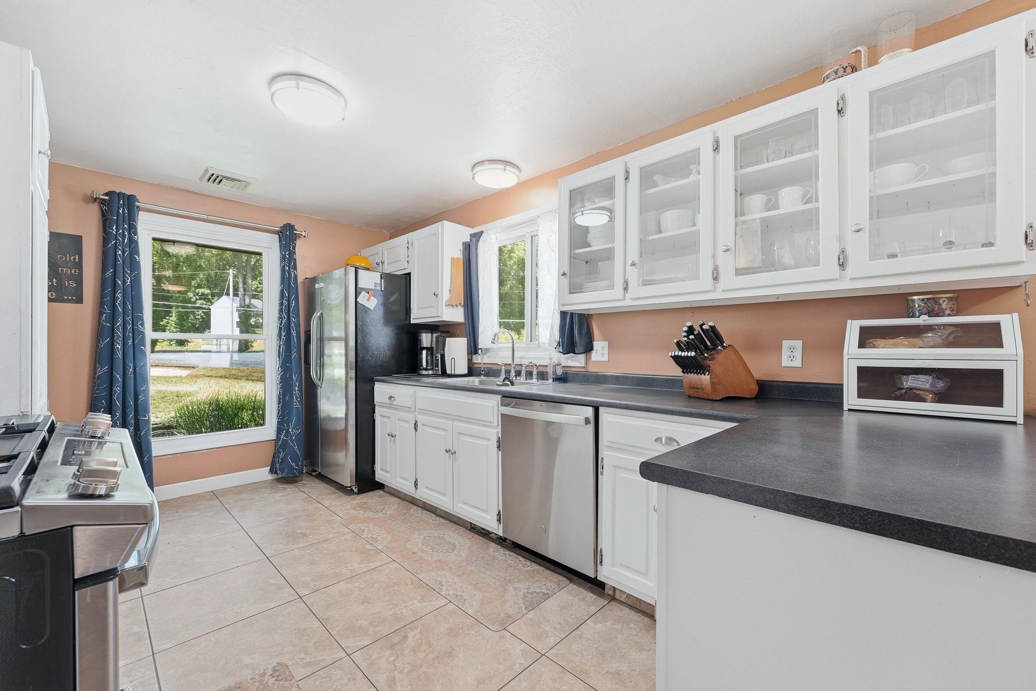 Kitchen featuring stainless steel appliances, white cabinetry, dark countertops, and ceramic tile flooring