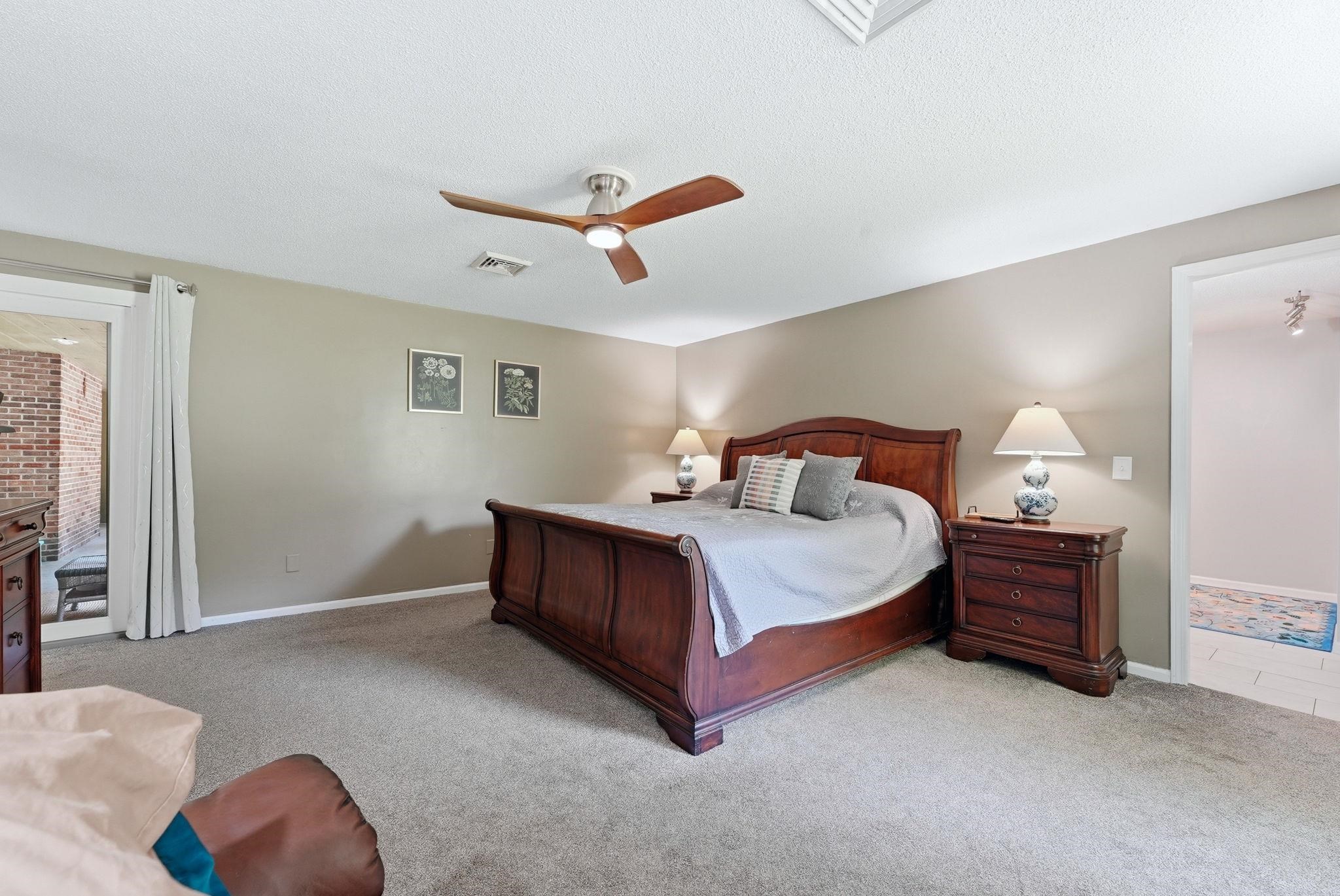 Spacious carpeted room featuring a ceiling fan, neutral wall paint, white trim, and a glass sliding door leading to an outdoor area with brickwork