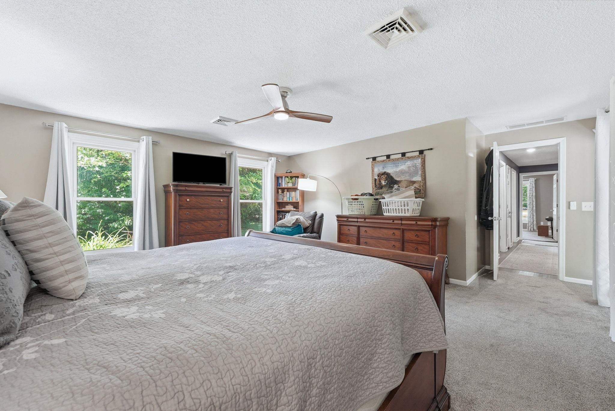 Carpeted bedroom featuring two large windows, a ceiling fan, and painted walls