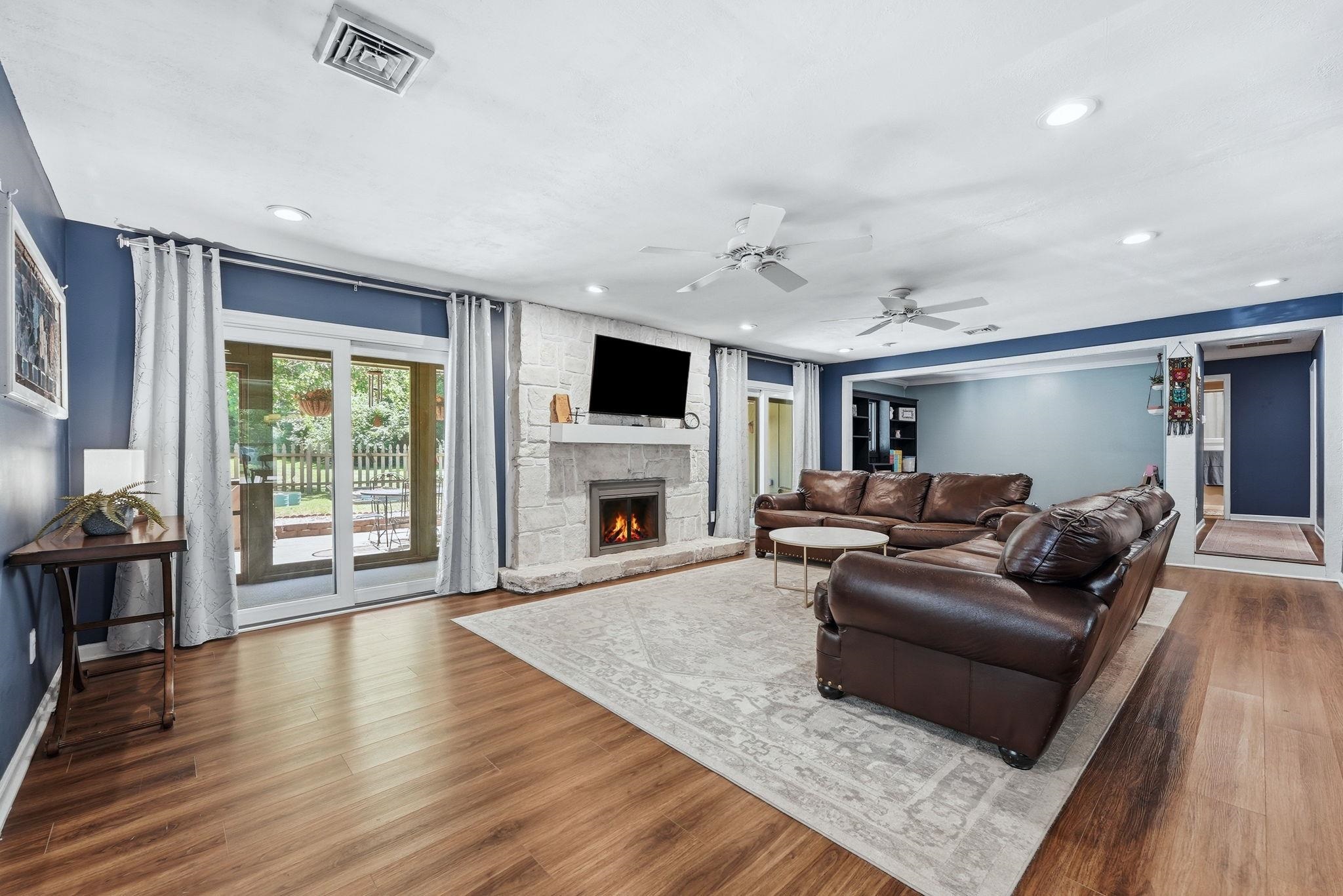 Living area featuring wood-finish flooring, a stone-clad fireplace with a hearth, and recessed lighting
