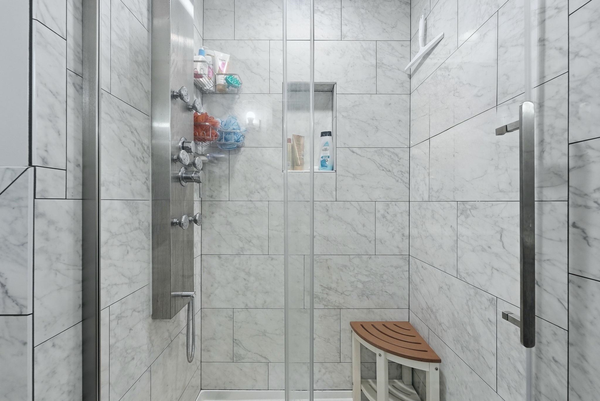 Shower enclosure featuring light-toned tile with subtle marbling, a stainless steel multi-function shower panel, and a built-in recessed shelf