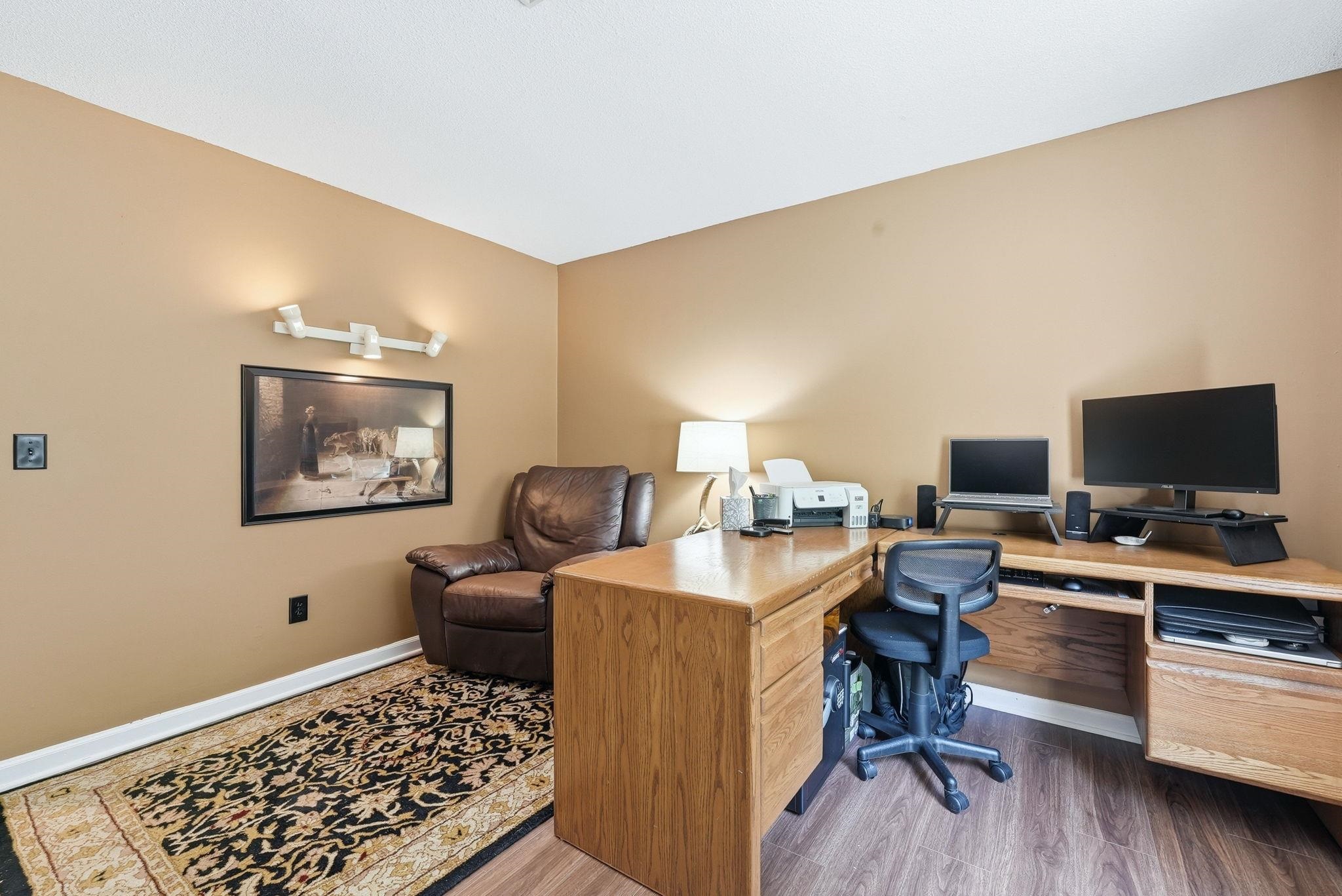 Dedicated room featuring neutral tone walls, wood-finish flooring, a built-in corner desk, wall sconce lighting, and white baseboards