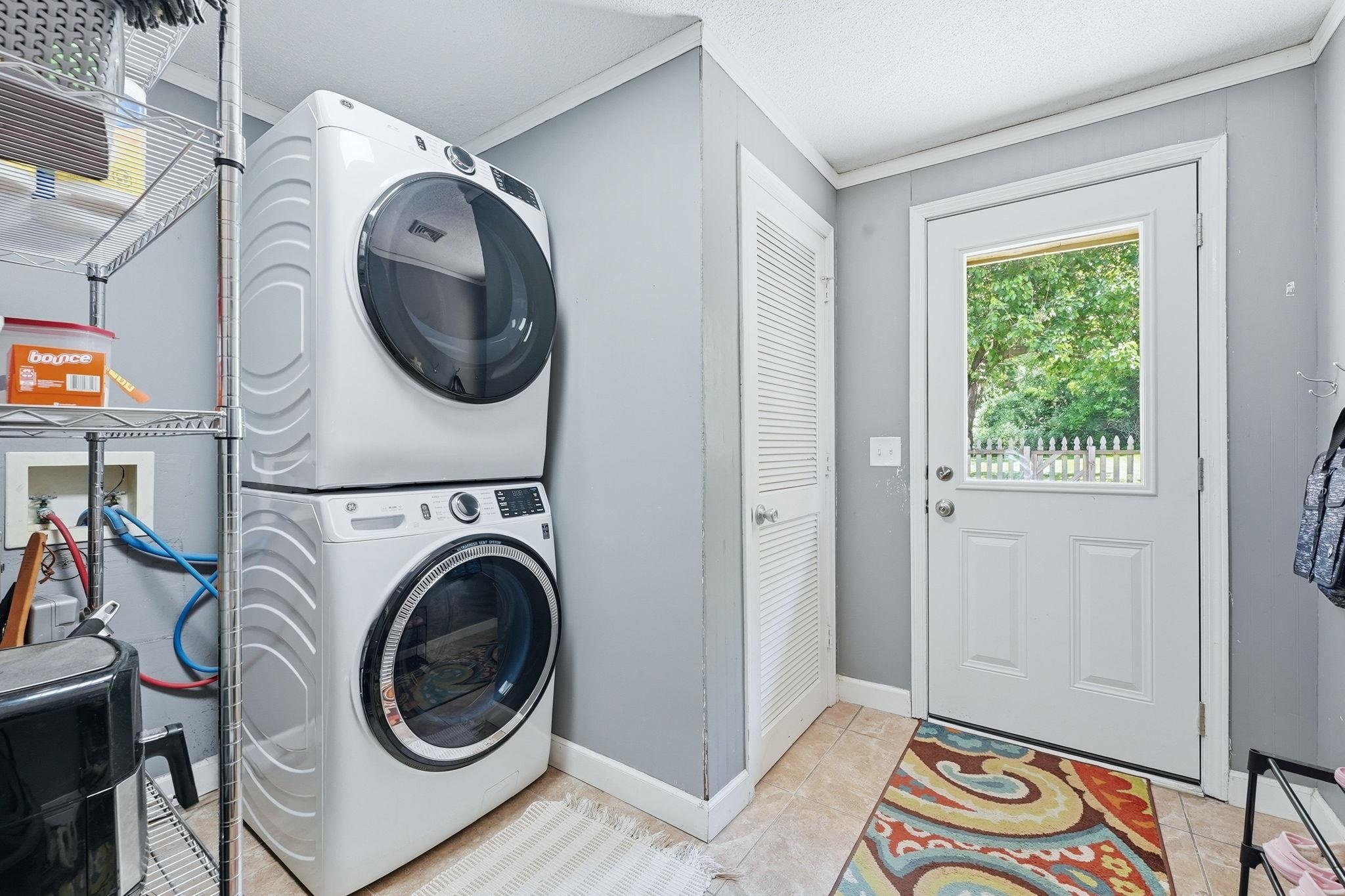 Dedicated laundry area featuring a stackable washer and dryer, tile flooring, and direct outdoor access through a glass-paneled door