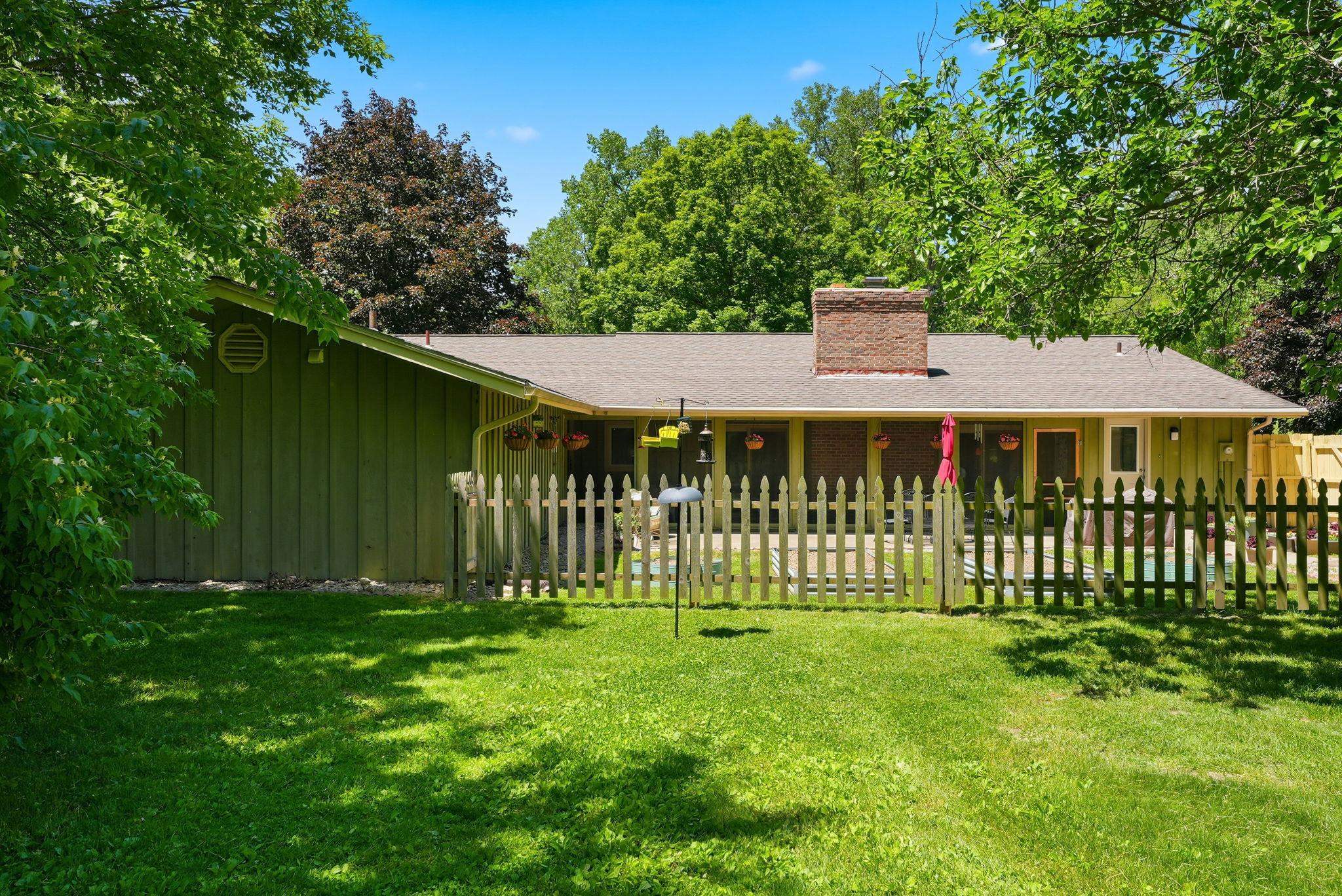 Expansive green lawn with mature trees and a fenced backyard featuring a patio area, brick chimney, and durable siding