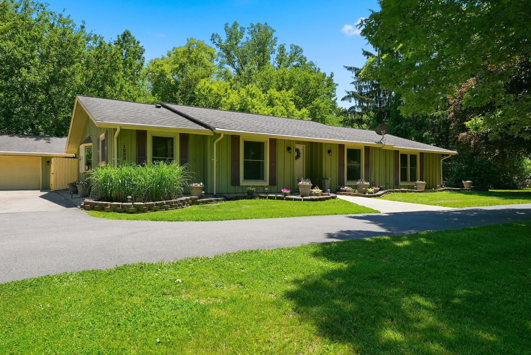 Ranch-style exterior with a pale green facade, dark brown window shutters, and a grey shingle roof