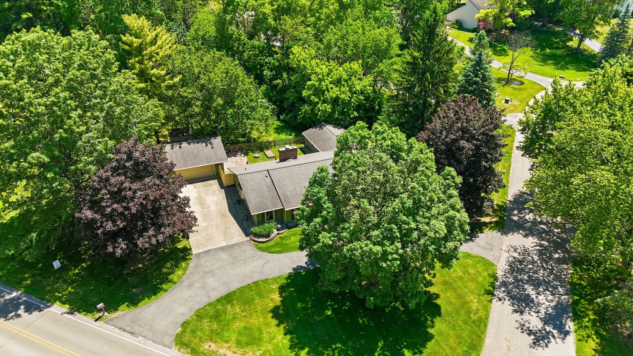 Aerial perspective showcasing a single-story residence with an attached garage, a long paved driveway, and mature landscaping
