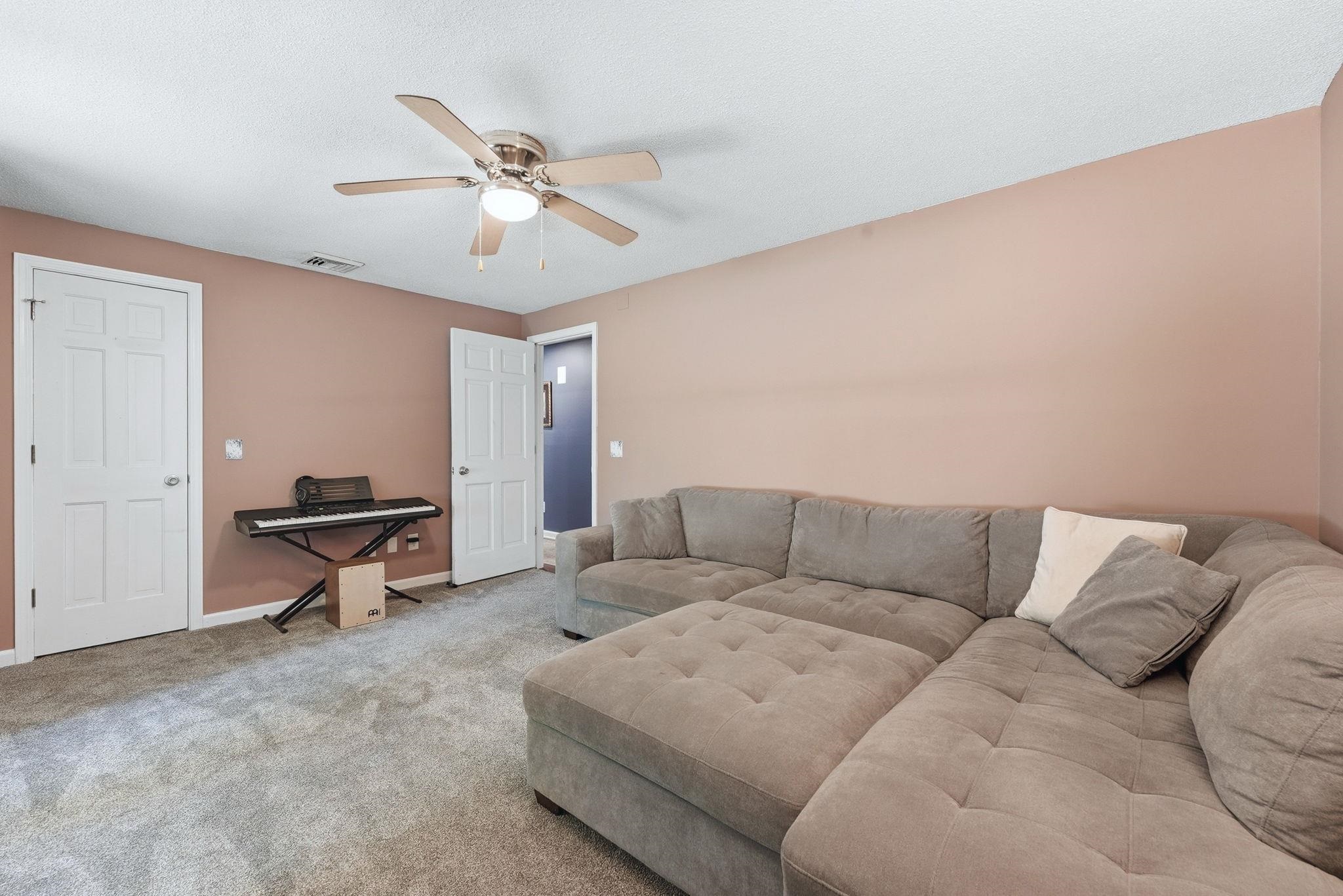 Carpeted room with a ceiling fan, two white paneled doors, and light pink walls