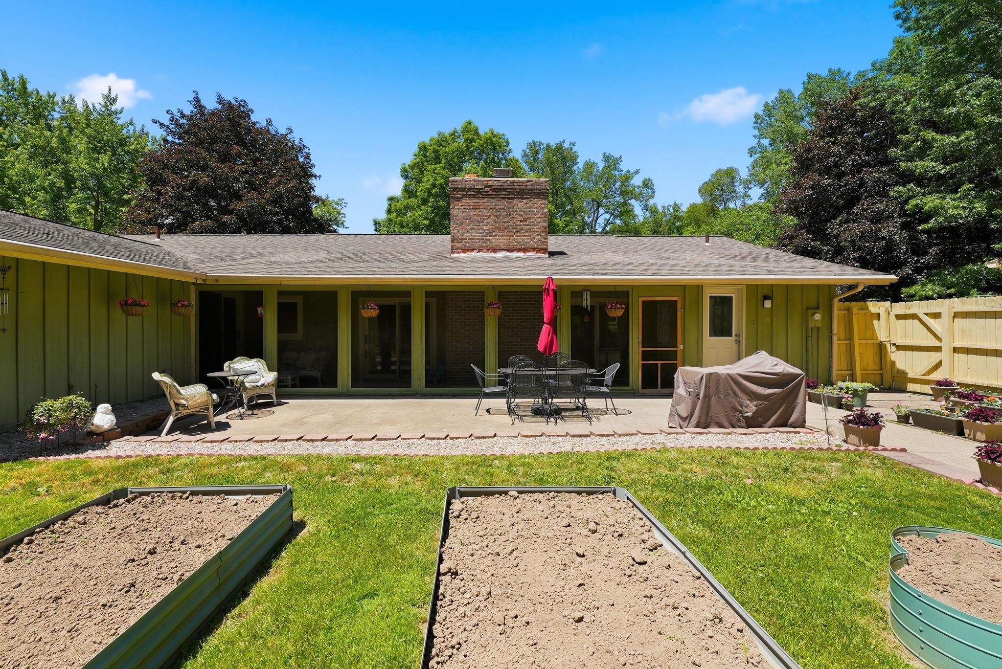 Expansive backyard featuring a stone patio, brick chimney, and raised garden beds