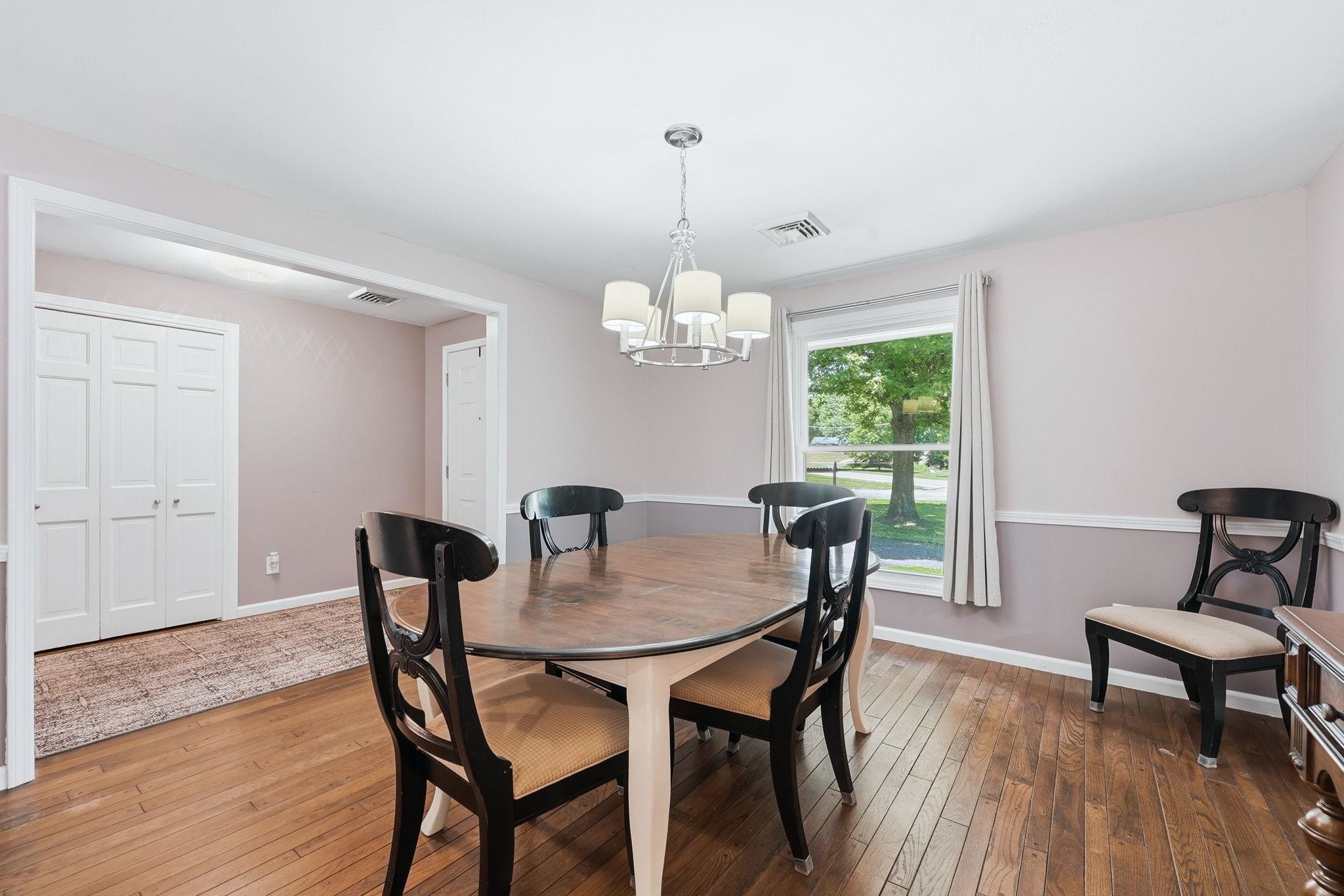 Hardwood flooring throughout, featuring a modern chandelier, a large picture window with outdoor scenery, and a chair rail molding