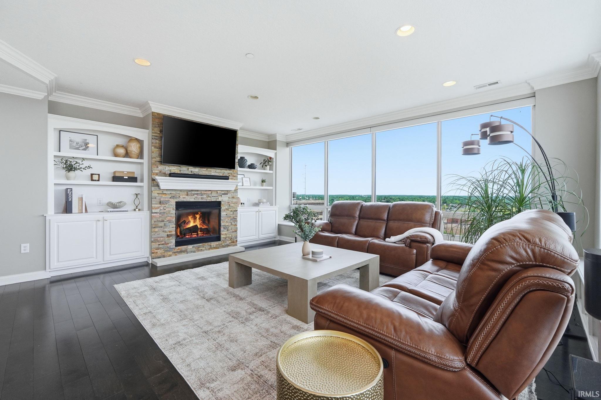 Living room featuring a stone fireplace with a white mantel, built-in shelving, dark wood-finish flooring, recessed lighting, and floor-to-ceiling windows