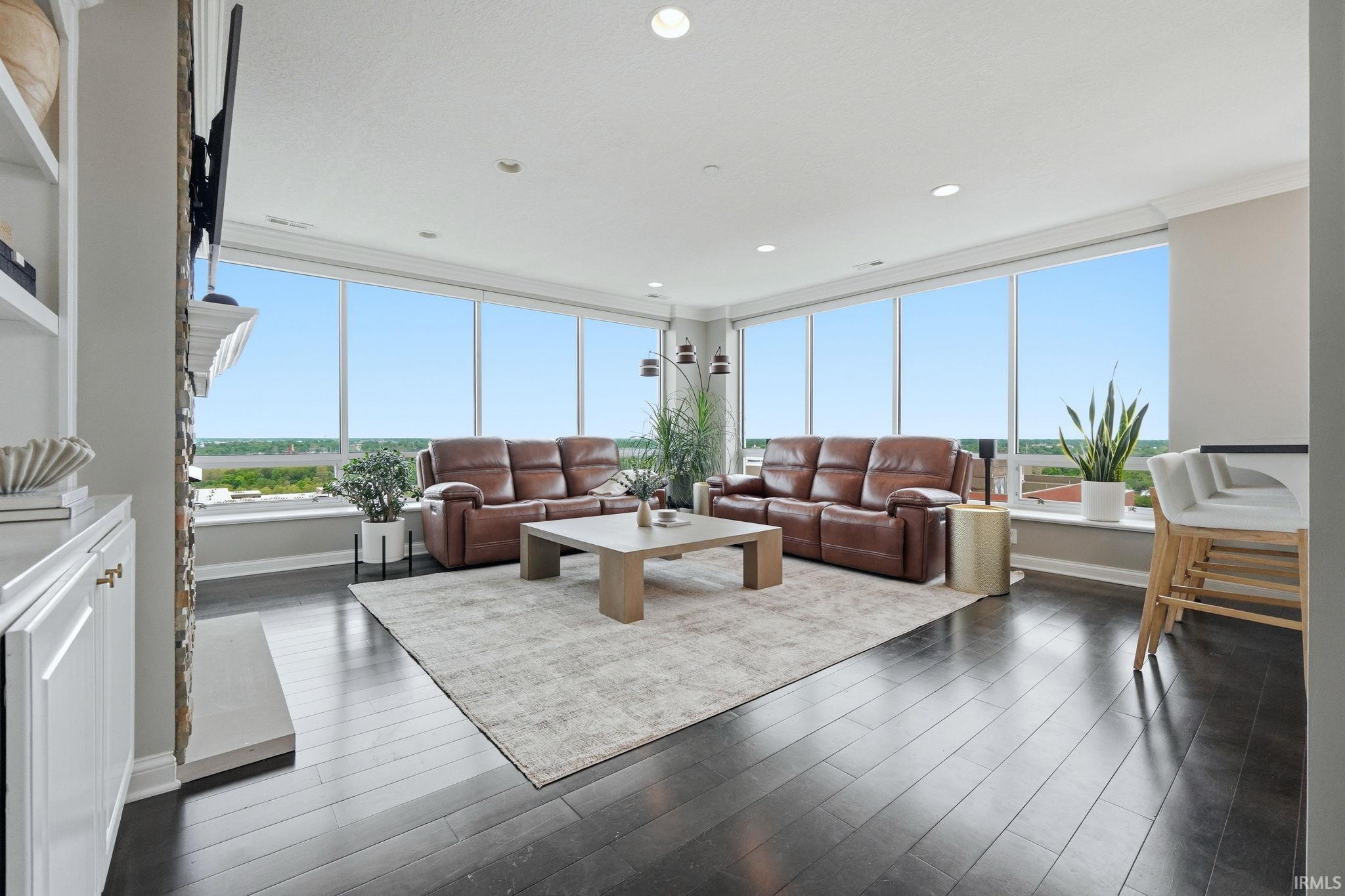 Living area featuring expansive windows, dark wood-finish flooring, recessed lighting, white built-in shelving, and a stone-clad fireplace surround