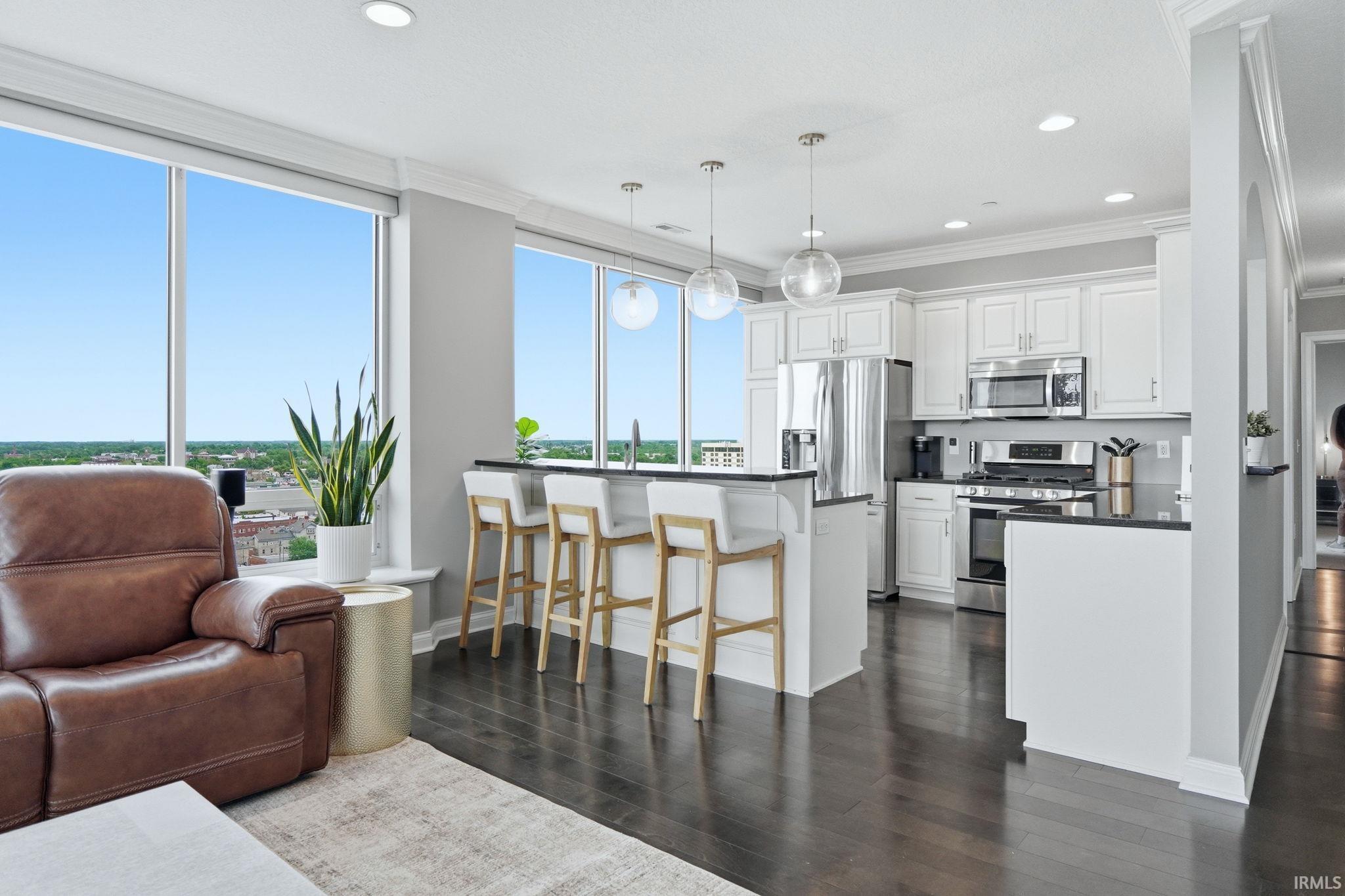 Open-concept kitchen featuring white cabinetry, stainless steel appliances, dark countertops, and a bar-height island with pendant lighting