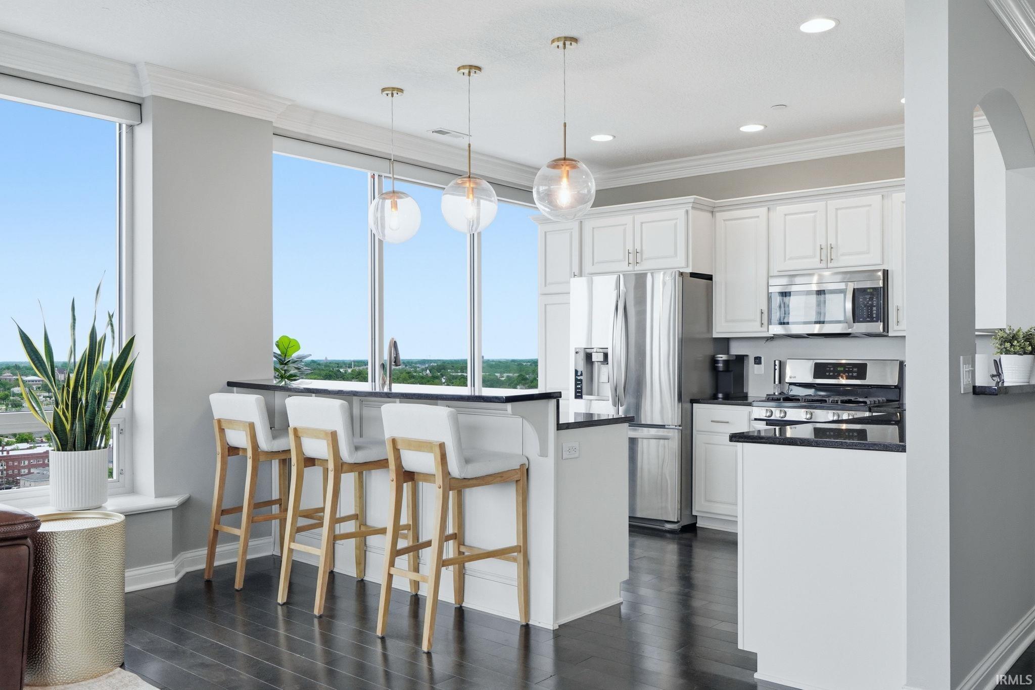 Gourmet kitchen featuring stainless steel appliances, white cabinetry, dark countertops, and wood-finish flooring
