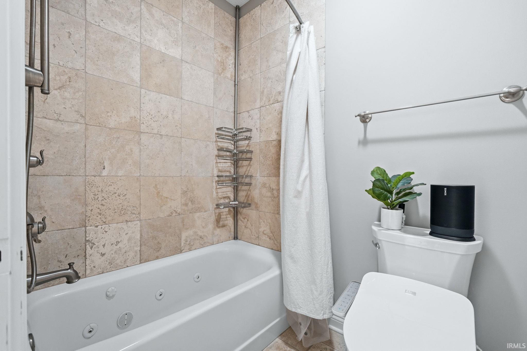 Bathroom featuring a jetted bathtub, natural stone tile surround, brushed nickel fixtures, and a wall-mounted towel bar