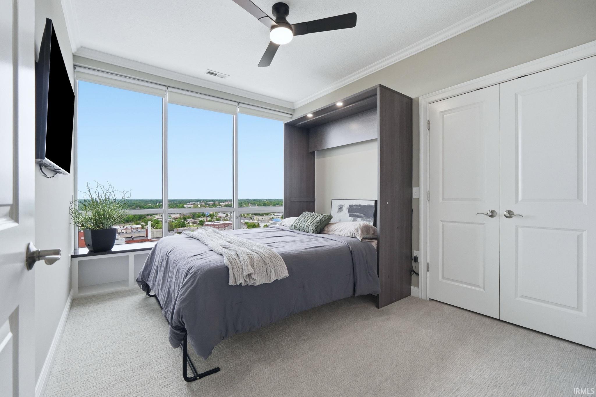 Room featuring floor-to-ceiling windows, built-in shelving, carpet flooring, a ceiling fan, and bi-fold closet doors