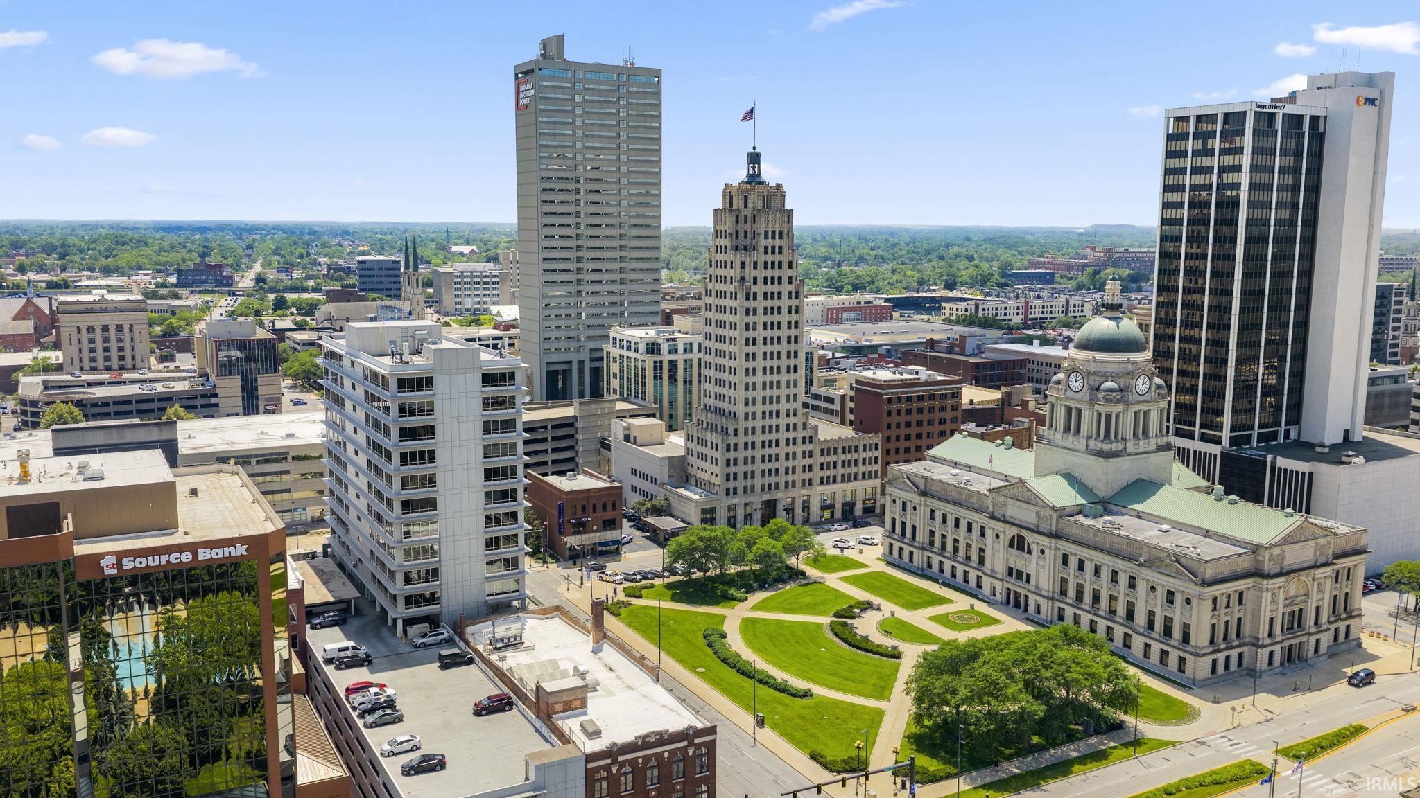 Elevated city perspective featuring diverse architectural styles, a prominent historic building with a domed cupola, multiple high-rise structures, a landscaped park area, and a network of urban streets