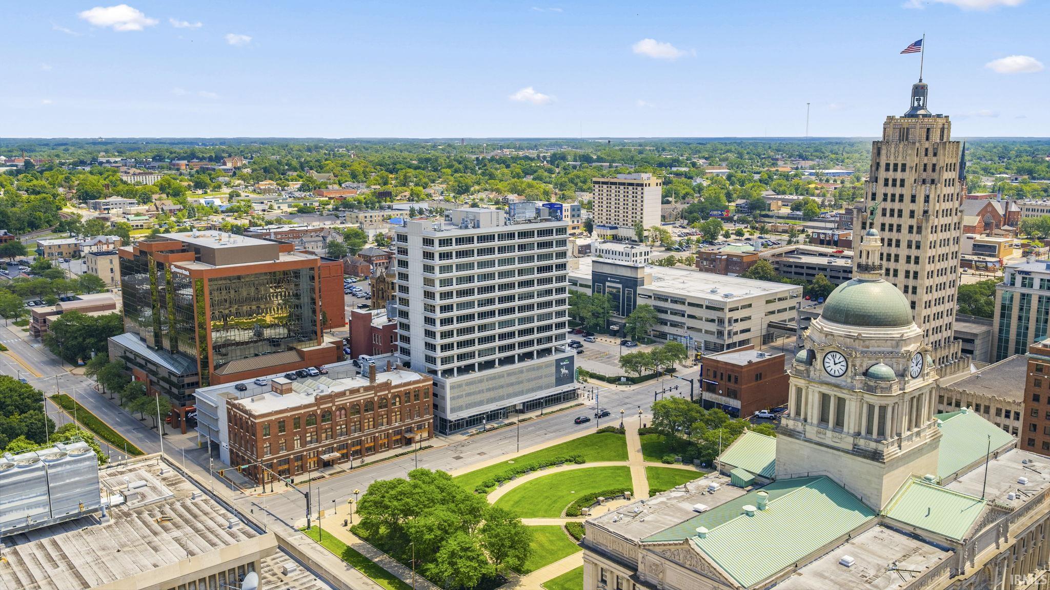 Cityscape featuring a mix of historic and modern architecture, including a domed building with a clock tower and a tall, light-colored building with a spire