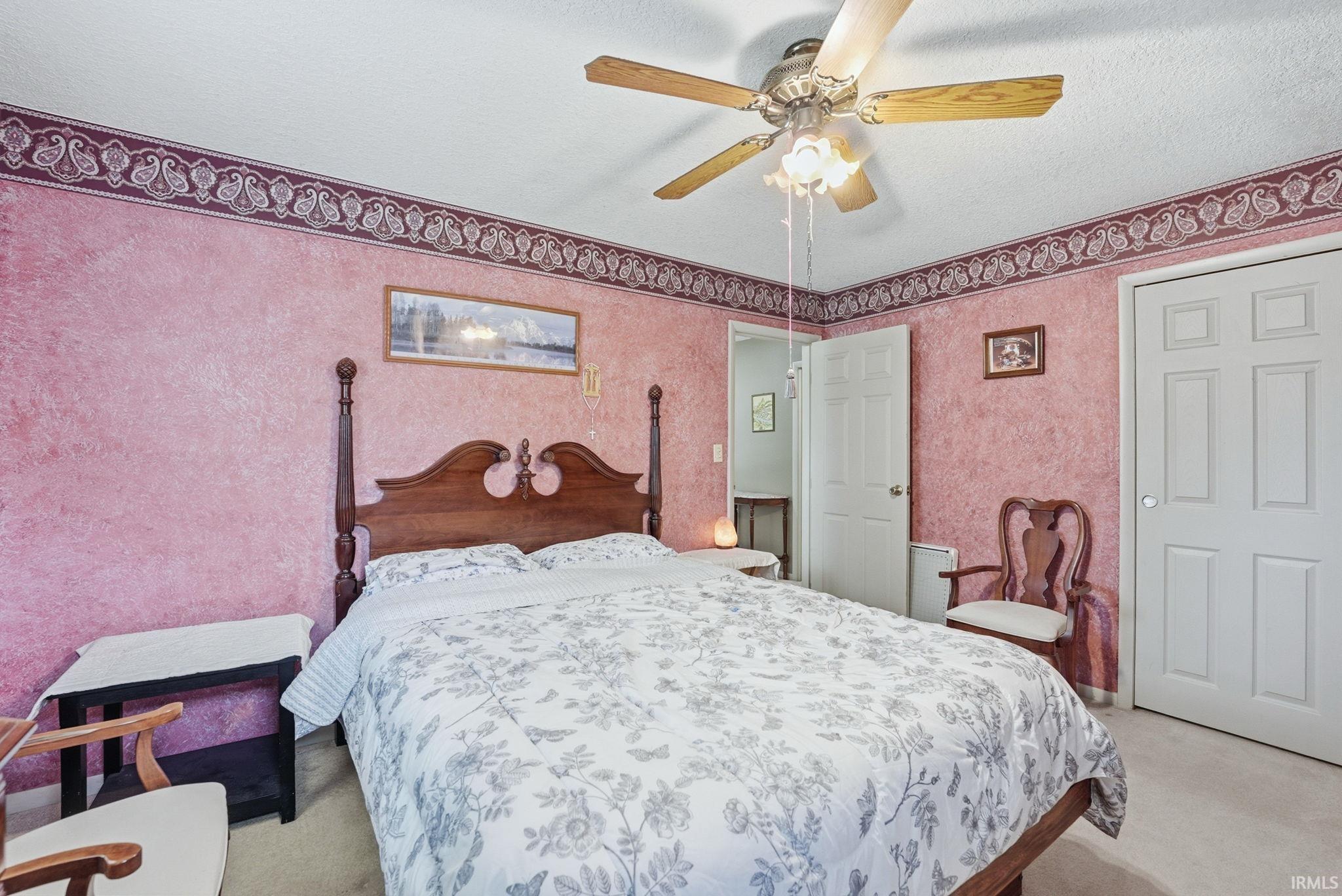 Bedroom featuring textured wall covering, a ceiling fan with integrated lighting, and carpet flooring