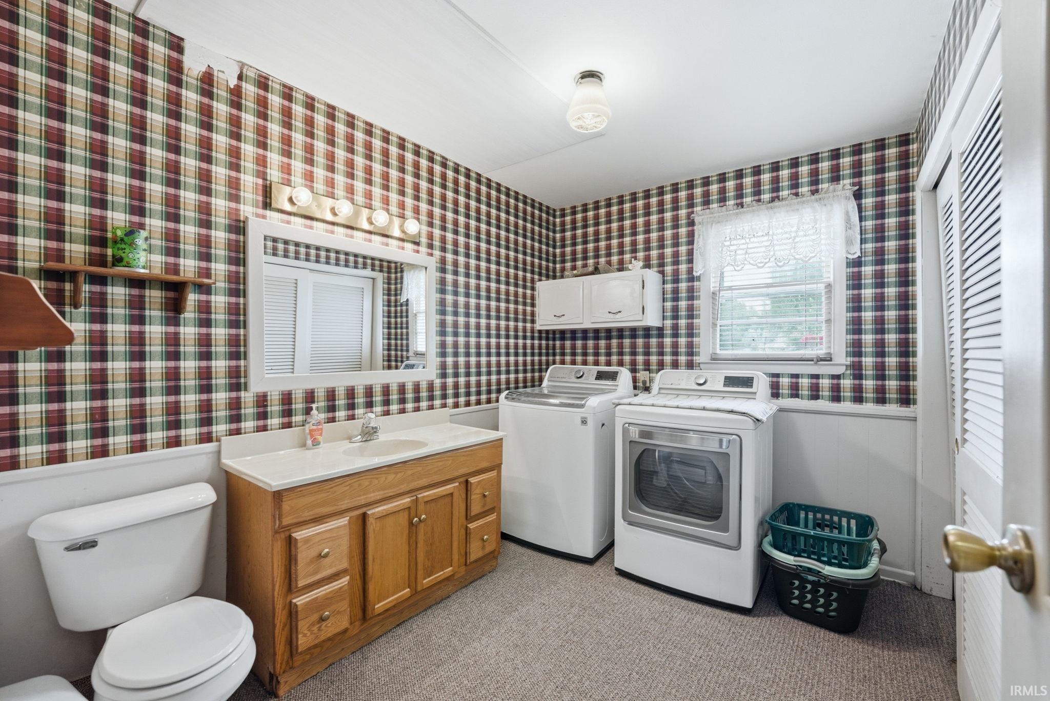 Laundry area featuring a wood-finish vanity with an integrated sink, wall-mounted cabinetry, a louvered door, and a window
