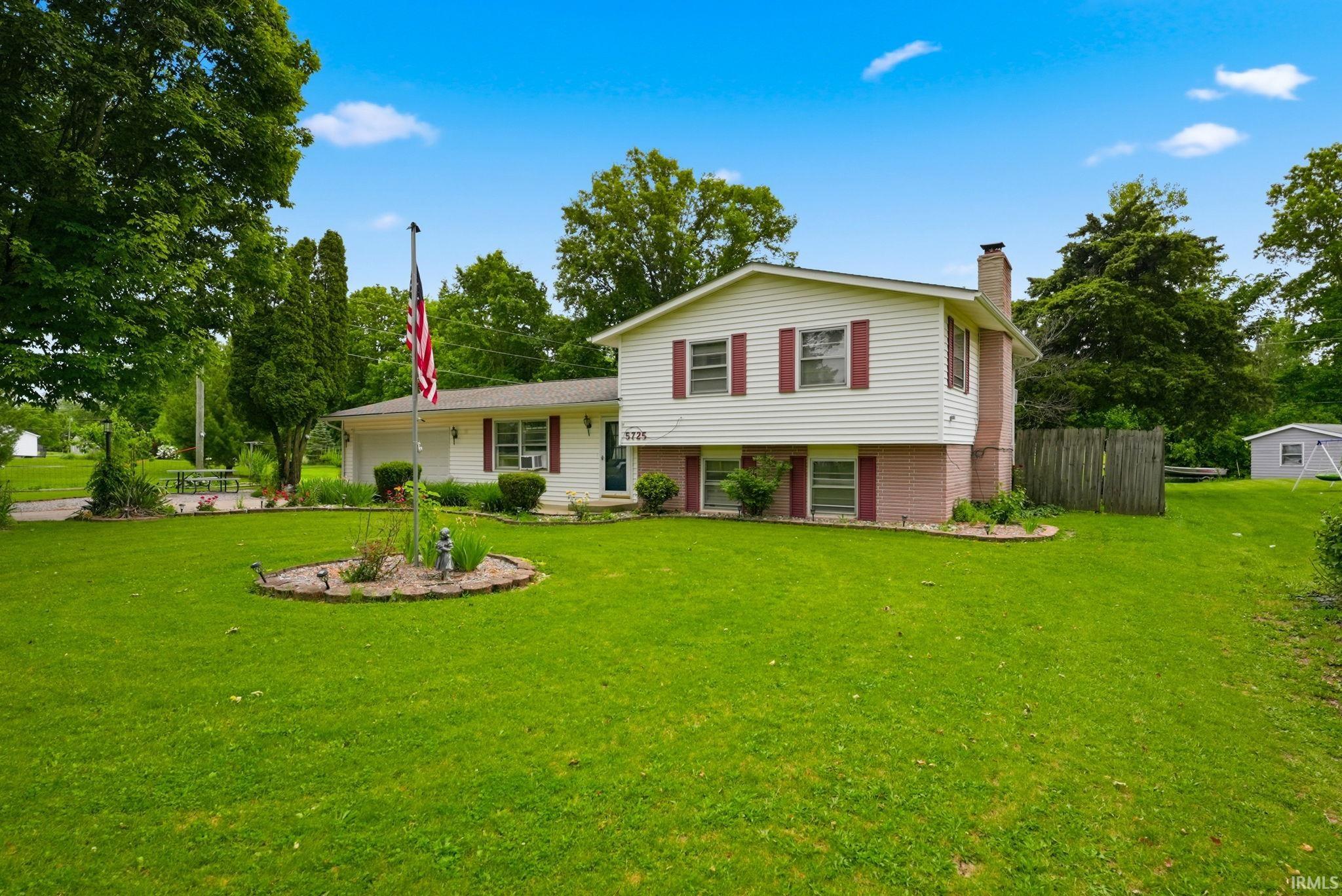 Split-level residence featuring white siding and red shutters, a brick chimney, and an attached garage